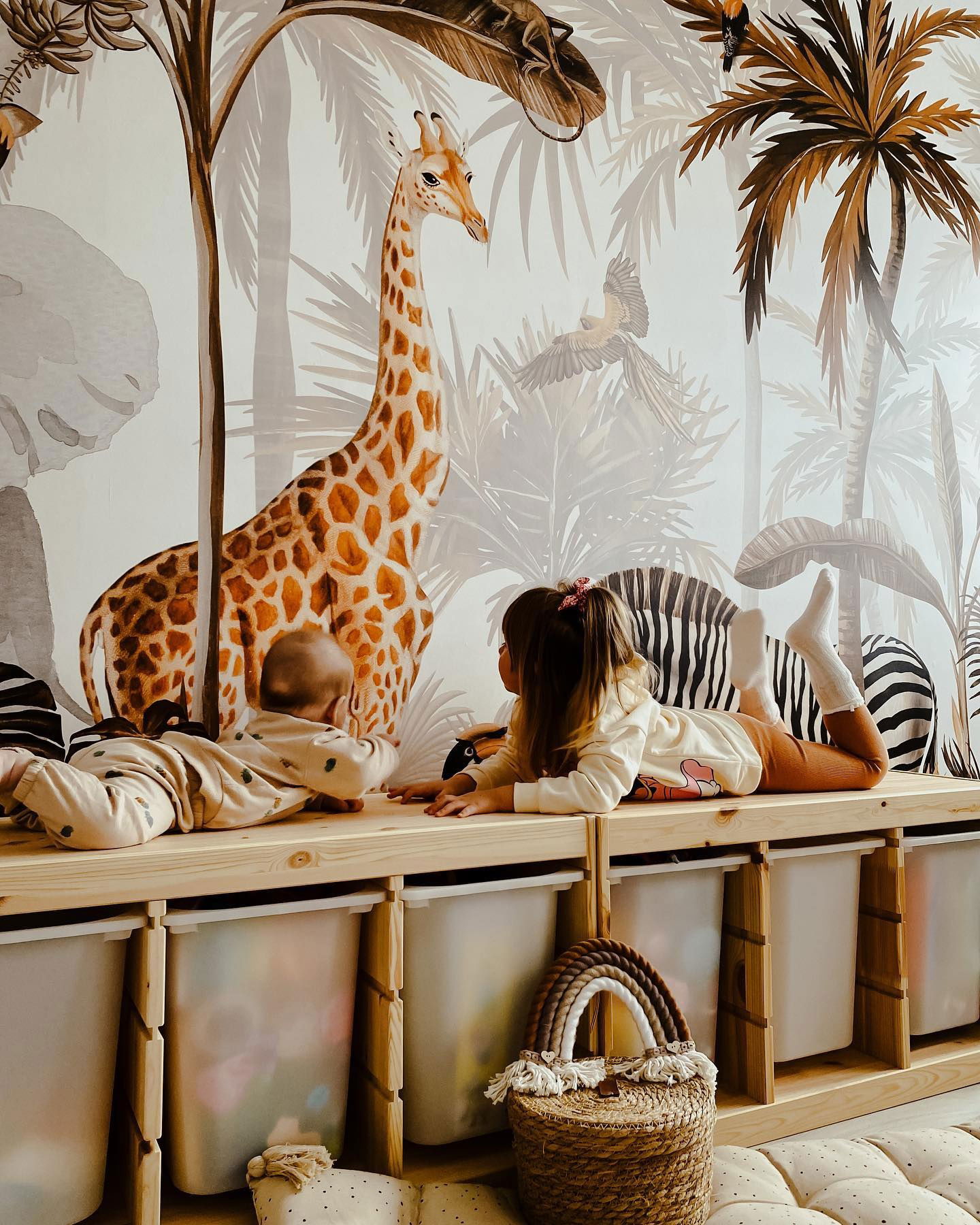 Twee kinderen liggen op een houten plank voor een jungle-behang.