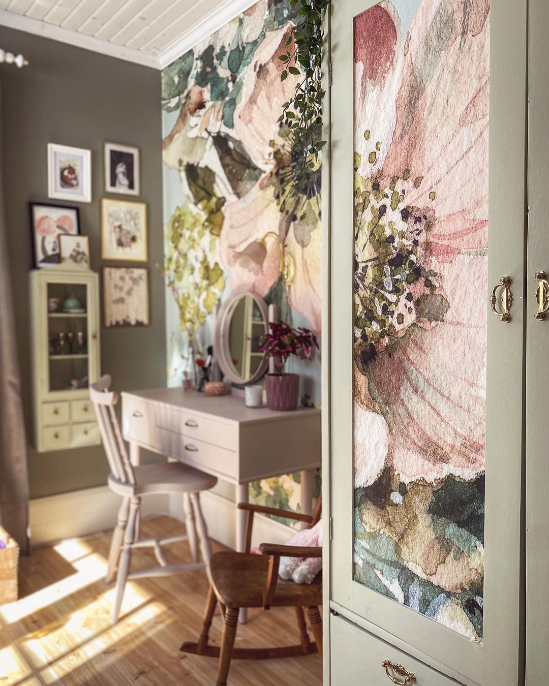 Schlafzimmer mit floraler Tapete, Schminktisch und bemaltem Kleiderschrank.