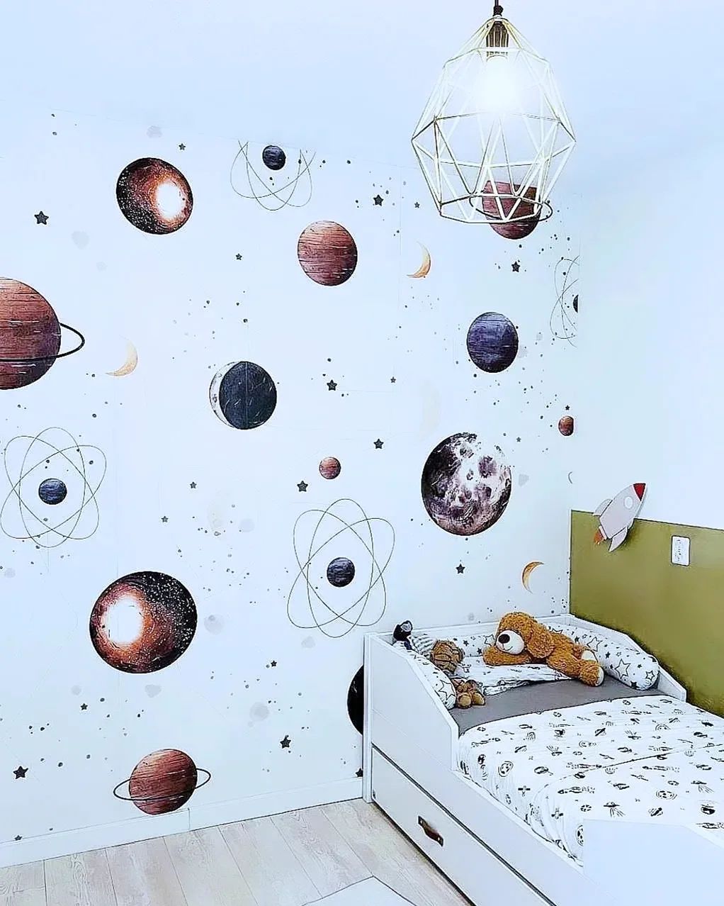 Child's bedroom with space-themed wall decals, white bed, and geometric pendant light.