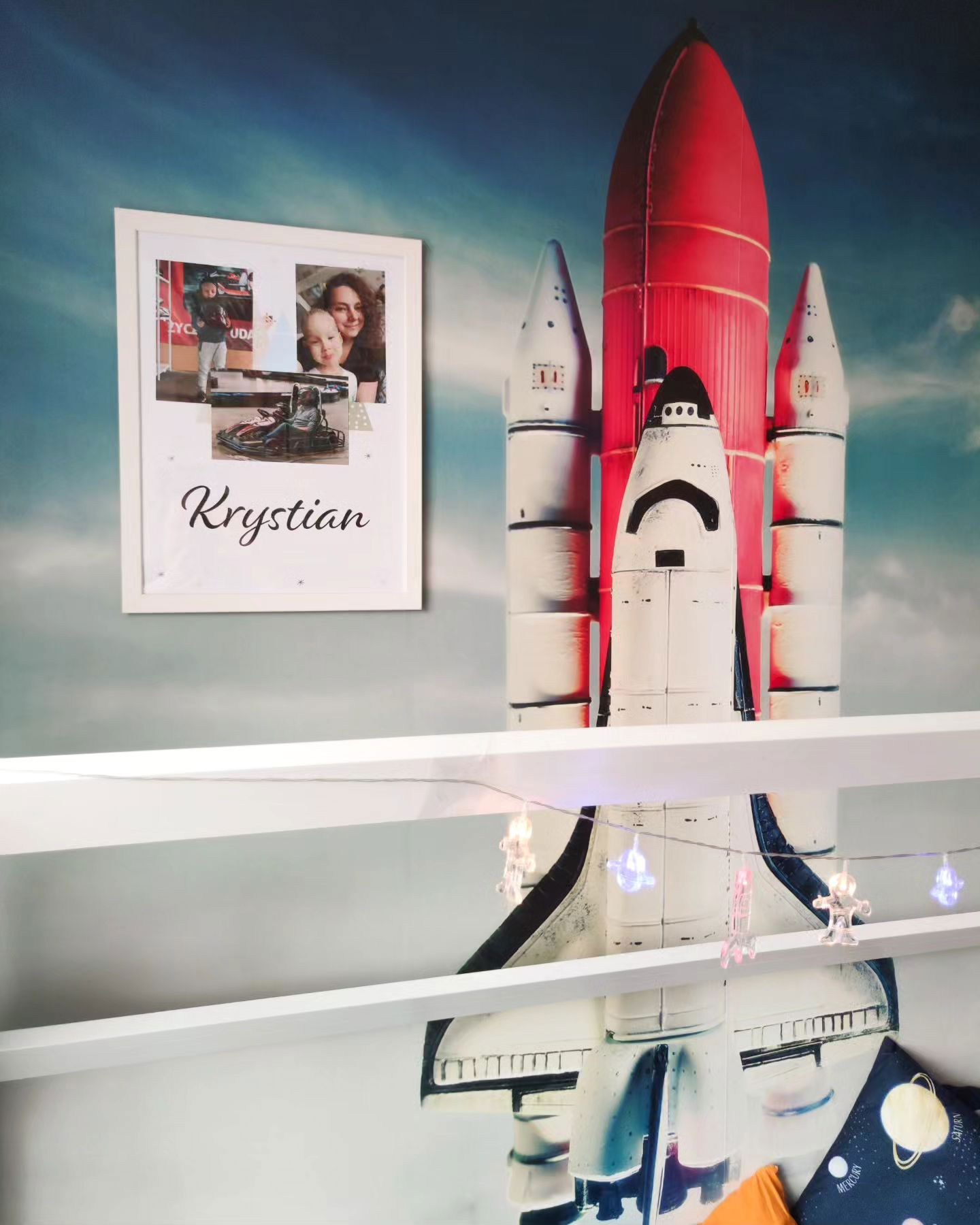 Kinderzimmer mit Raketendekor, Lichterketten und gerahmten Fotos mit der Aufschrift "Krystian".
