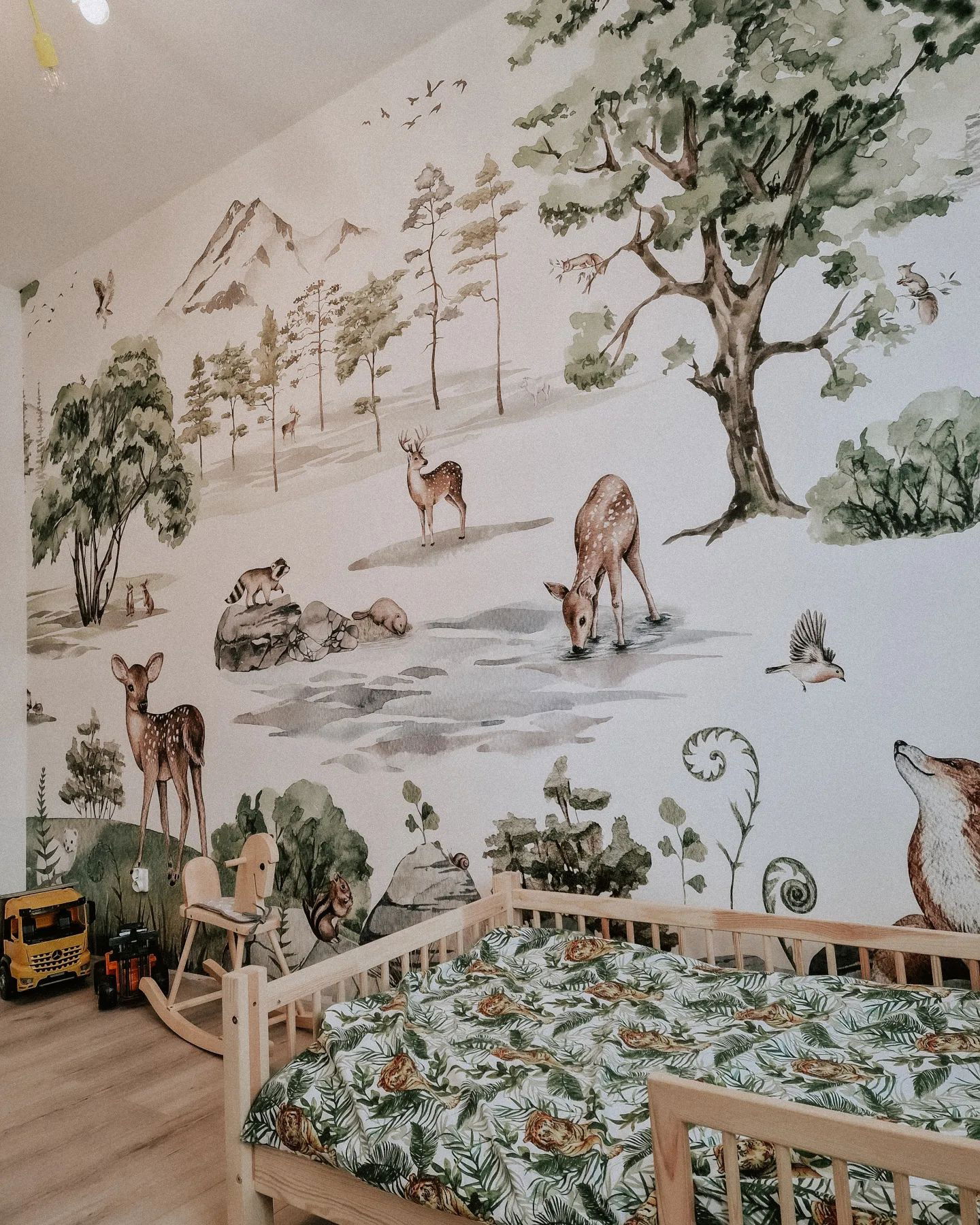 Child's room with forest mural, wooden bed with tiger-leaf bedding, and toys.