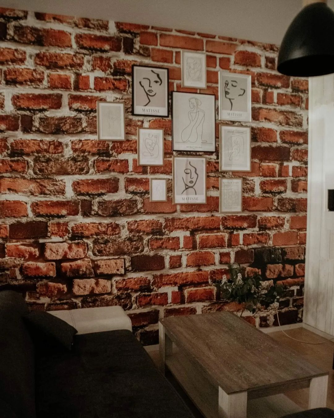 Living room with brick wallpaper, gallery wall of Matisse-style art, dark sofa, and wood coffee table.