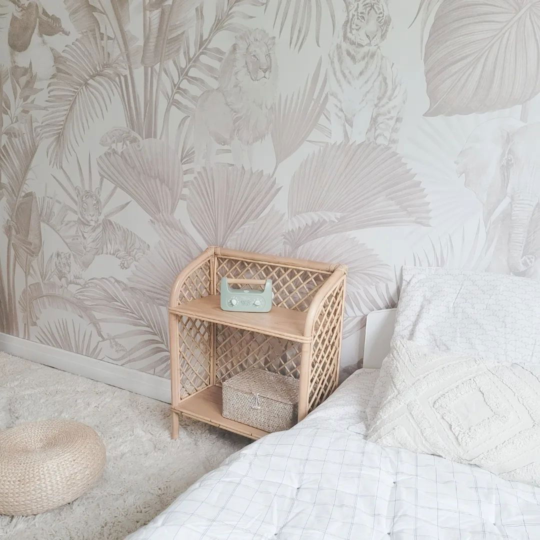Chambre avec papier peint jungle, table de chevet en rotin et literie blanche.