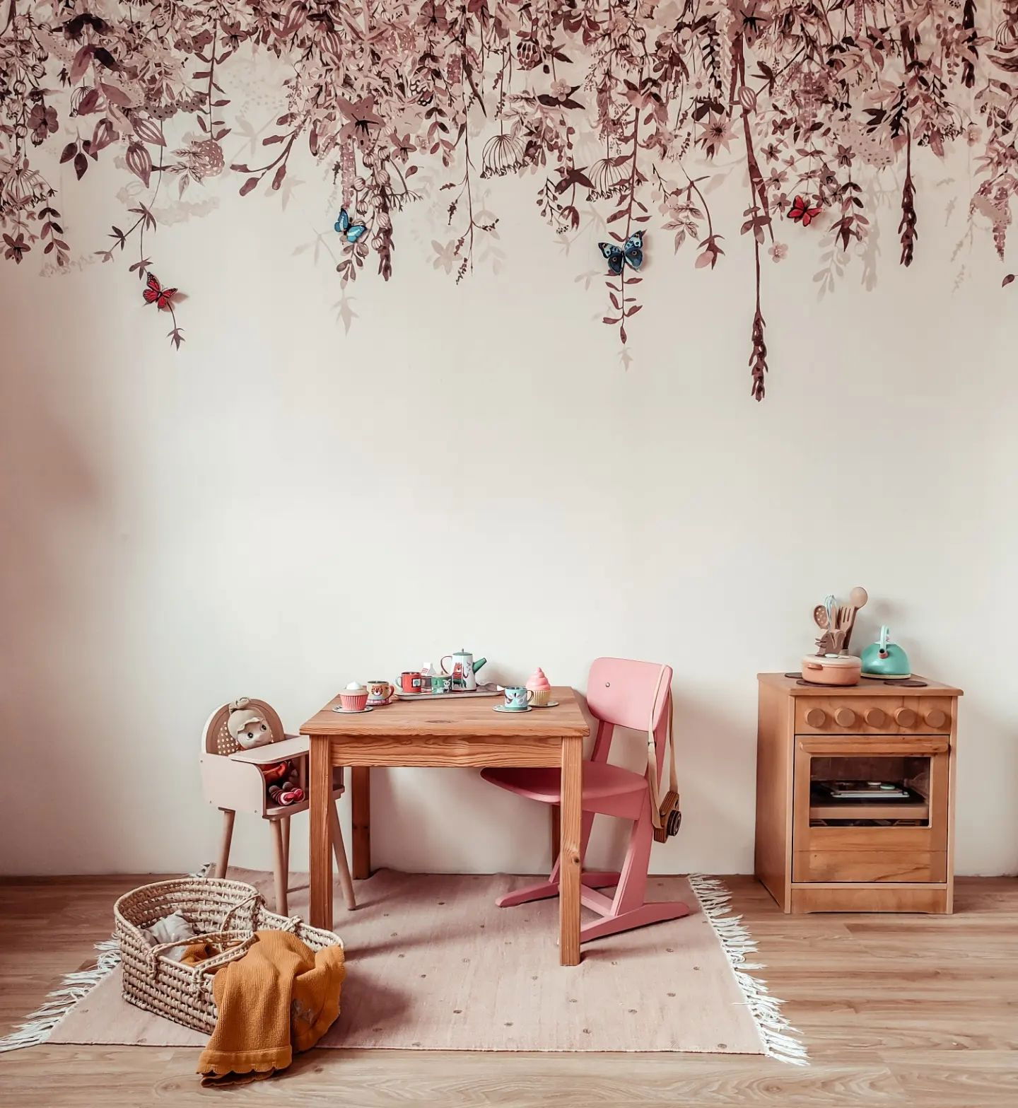 Playroom with wooden table, pink chair, toy stove, and floral wallpaper with butterflies.