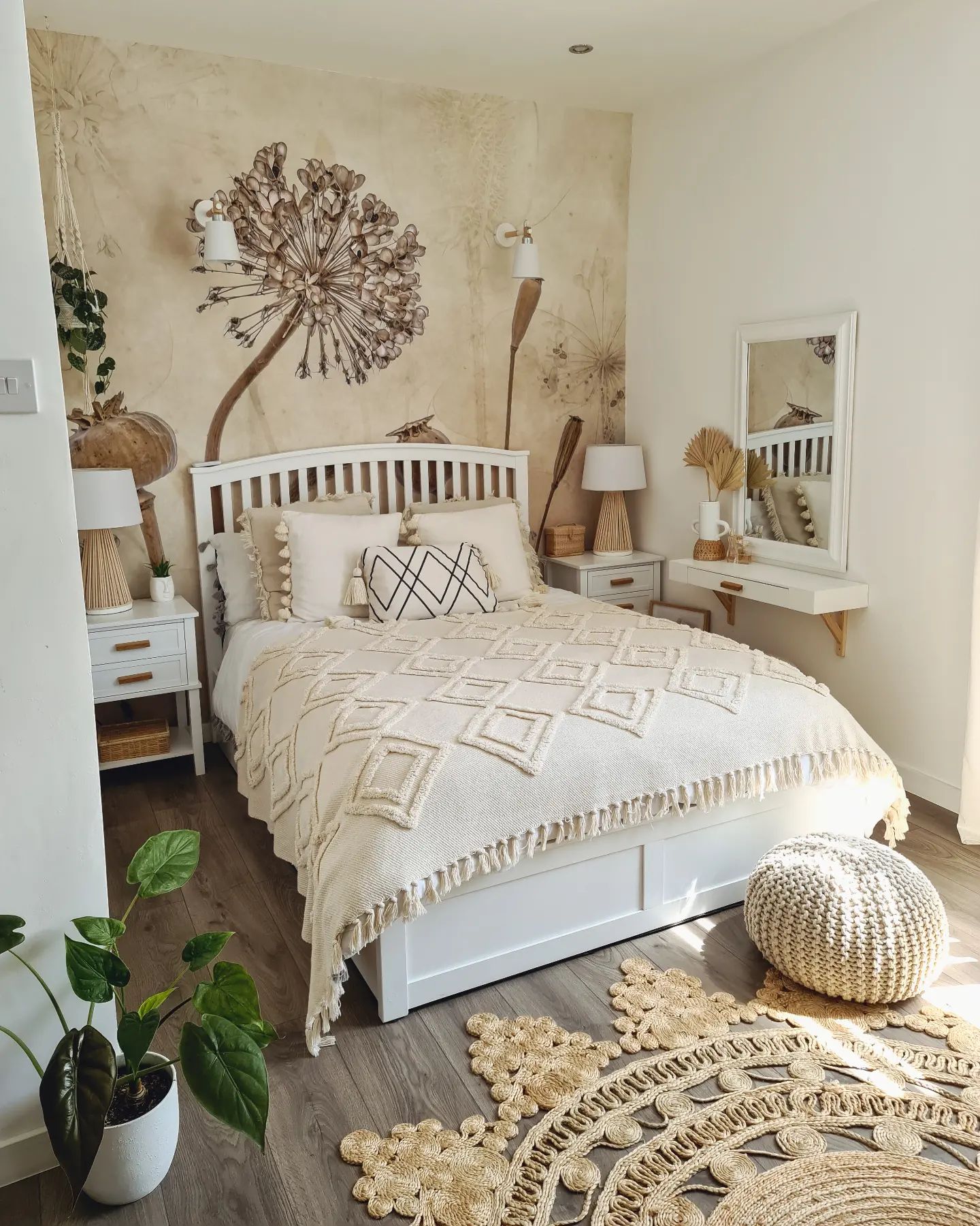 Chambre confortable avec lit blanc, tables de chevet et décoration. Un grand autocollant mural floral se trouve derrière le lit. Tapis et pouf en jute sur le sol.