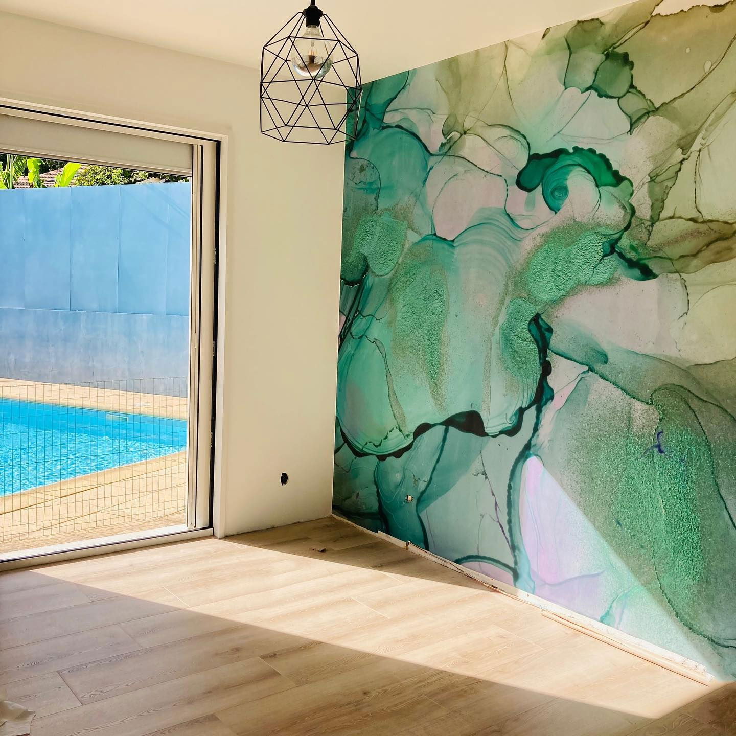 Room with green marble wallpaper, wood floors, and open door to a pool.