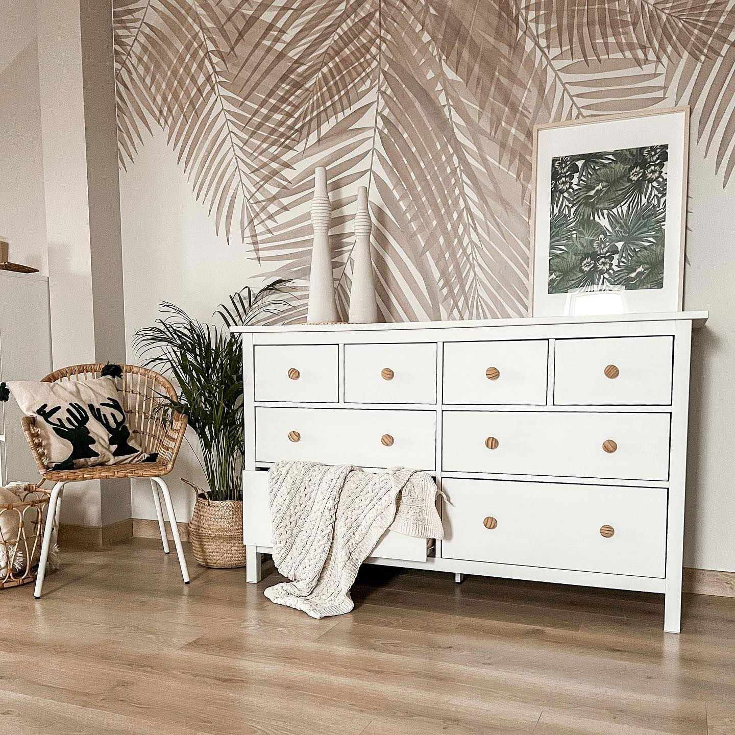 Interior de sala de estar con tocador blanco, papel tapiz tropical y silla de mimbre.