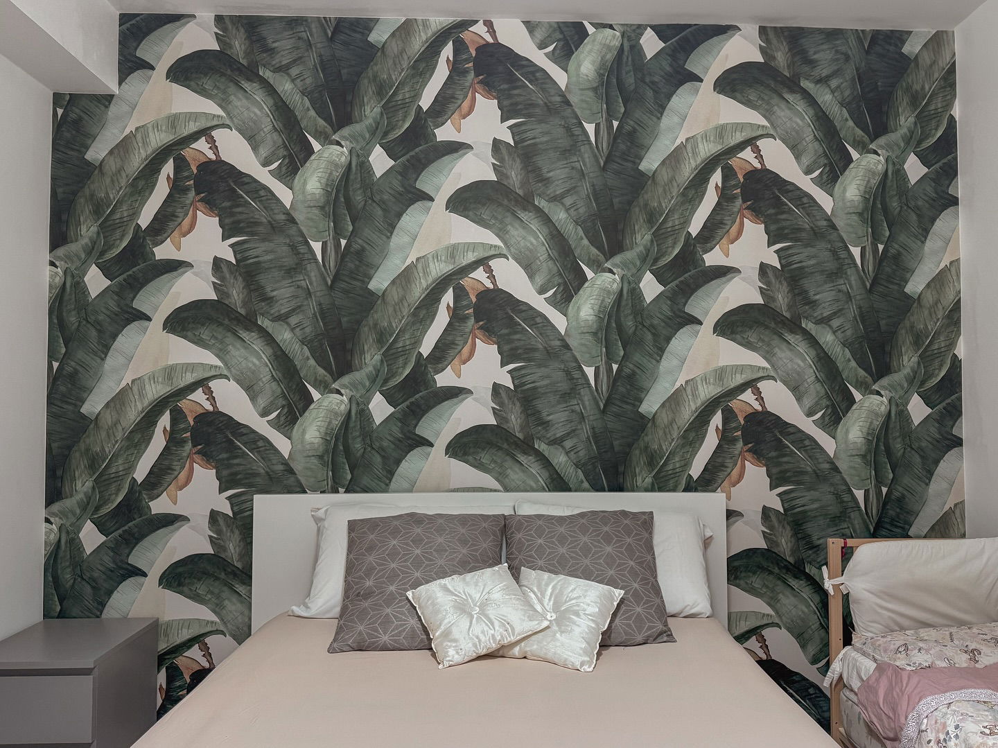 Bedroom with banana leaf wallpaper, white headboard, and neutral bedding.