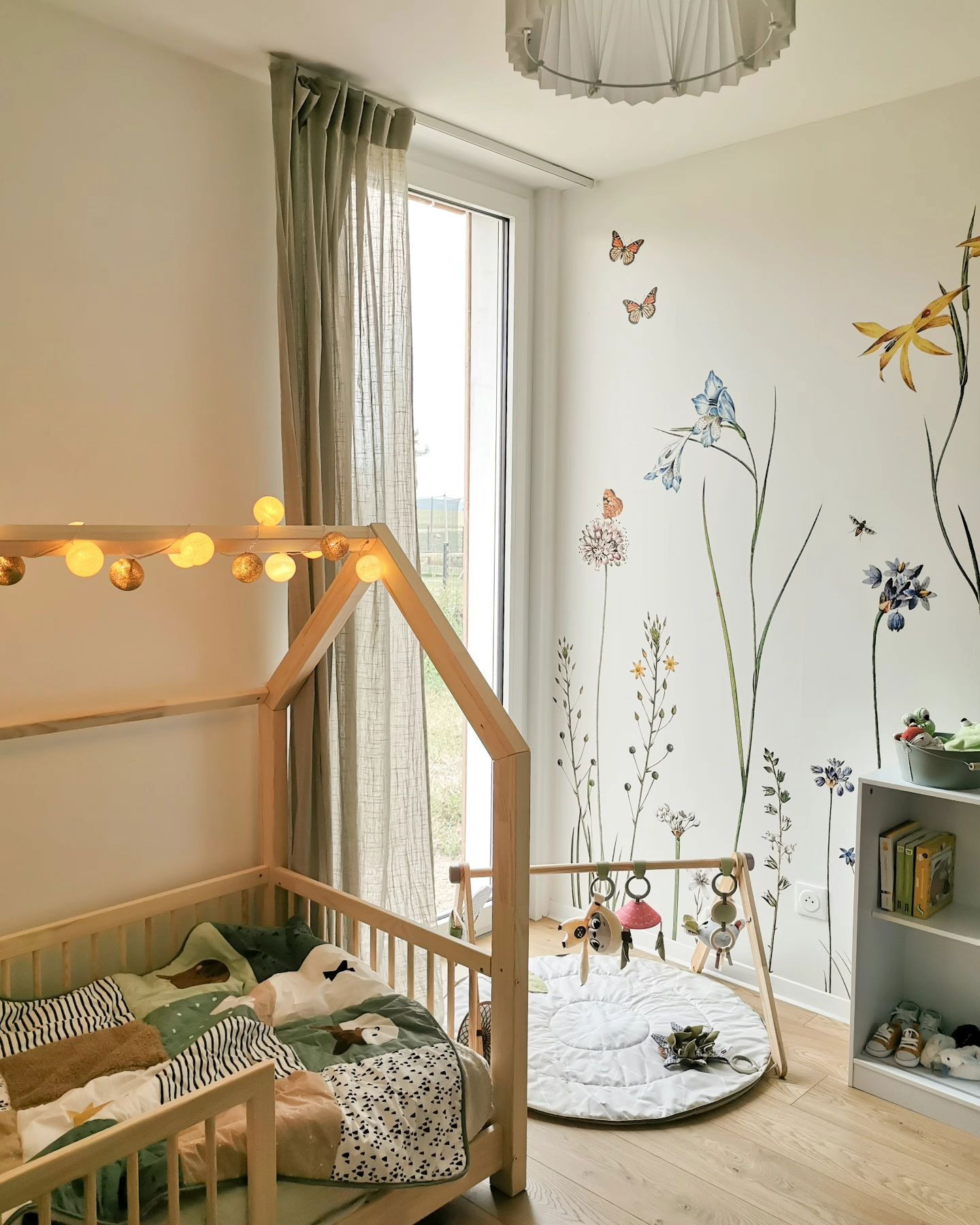 Nursery with wooden house bed, floral wall decals, and play gym.