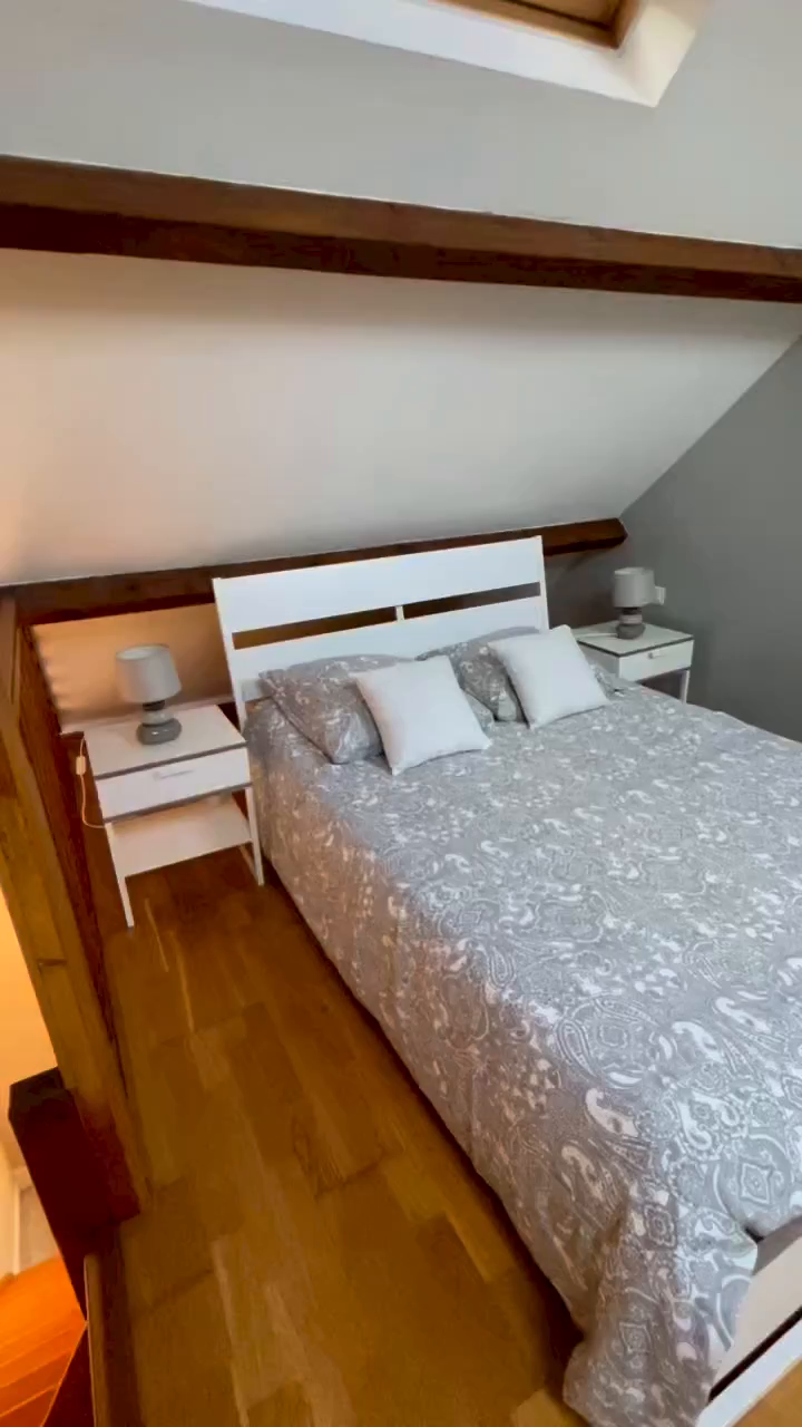 Attic bedroom with white bed frame, paisley bedding, and matching nightstands.