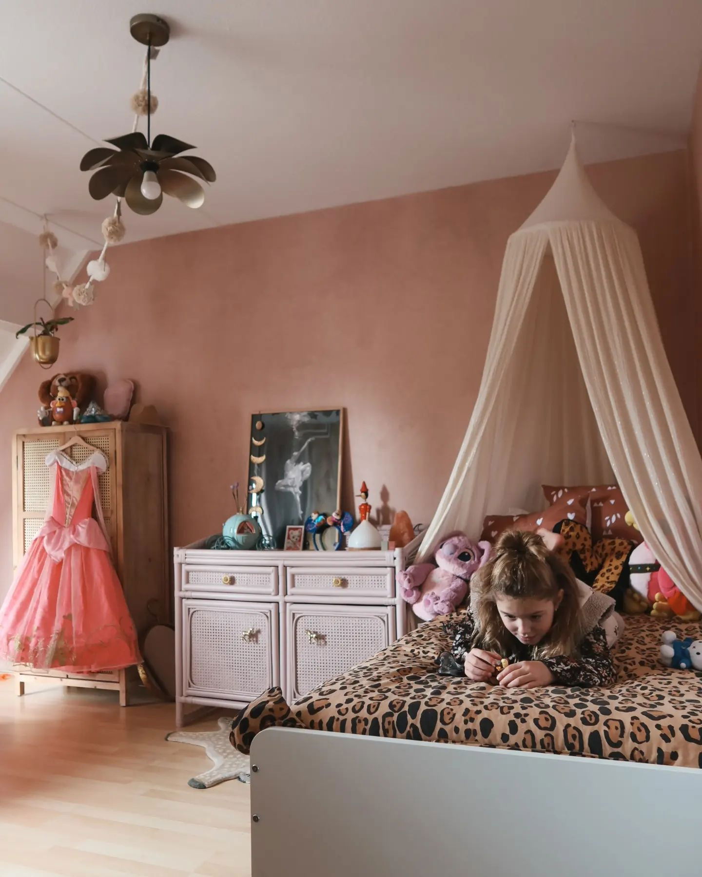 Child lies on a leopard print bed in a pink bedroom with a canopy and pink princess dress.