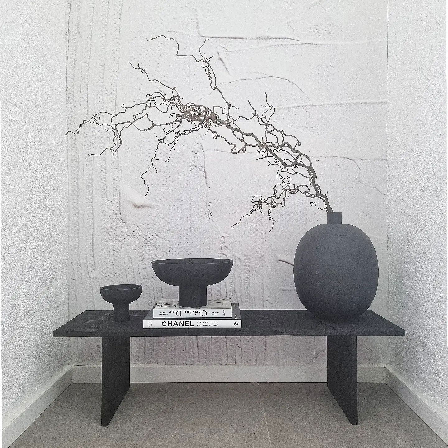 Minimalistische Einrichtung: schwarze Bank mit Schalen, Vase mit Zweigen und Chanel-Büchern.