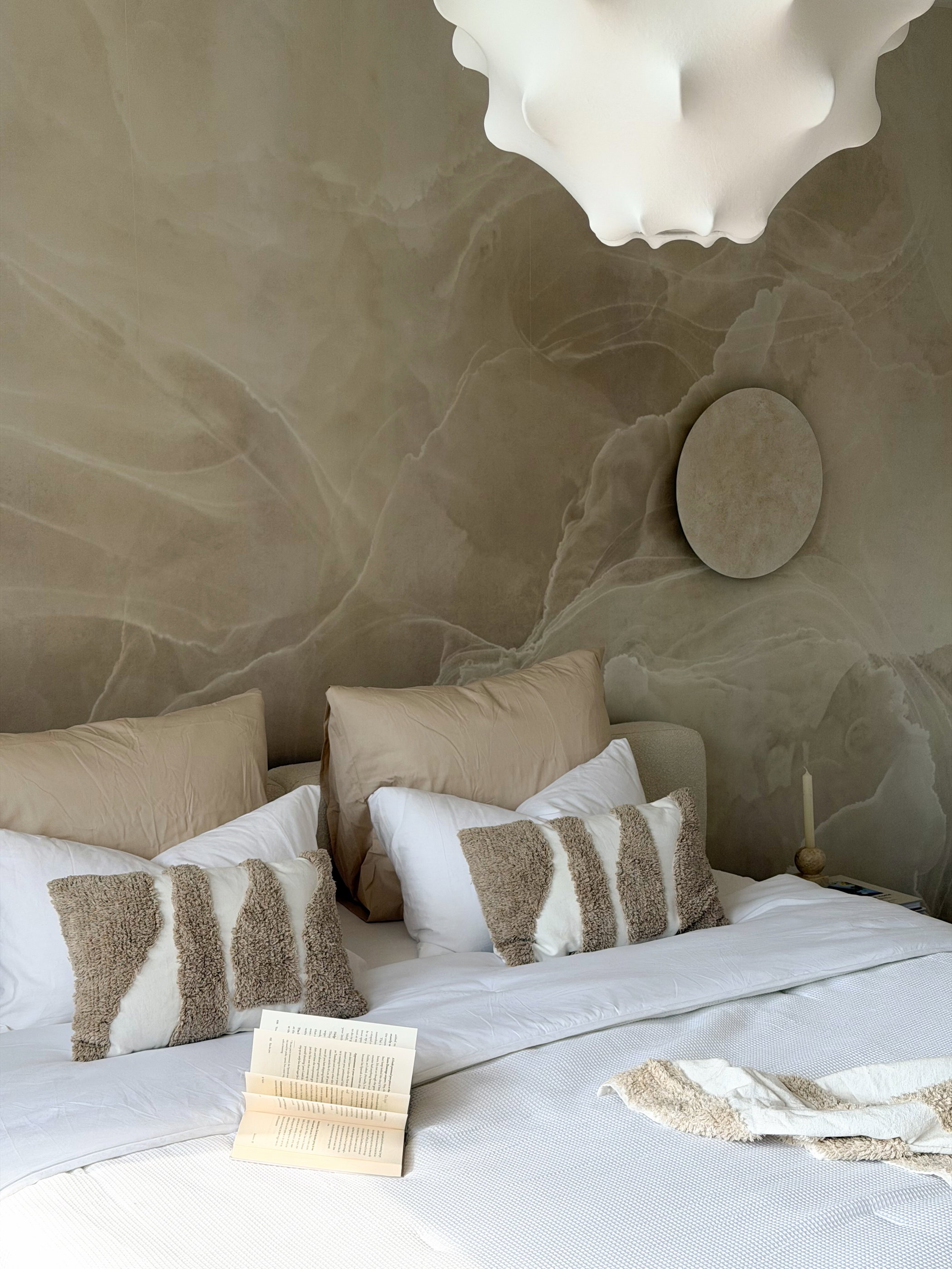 Bed with white linens, decorative pillows, and a marble-patterned wall.