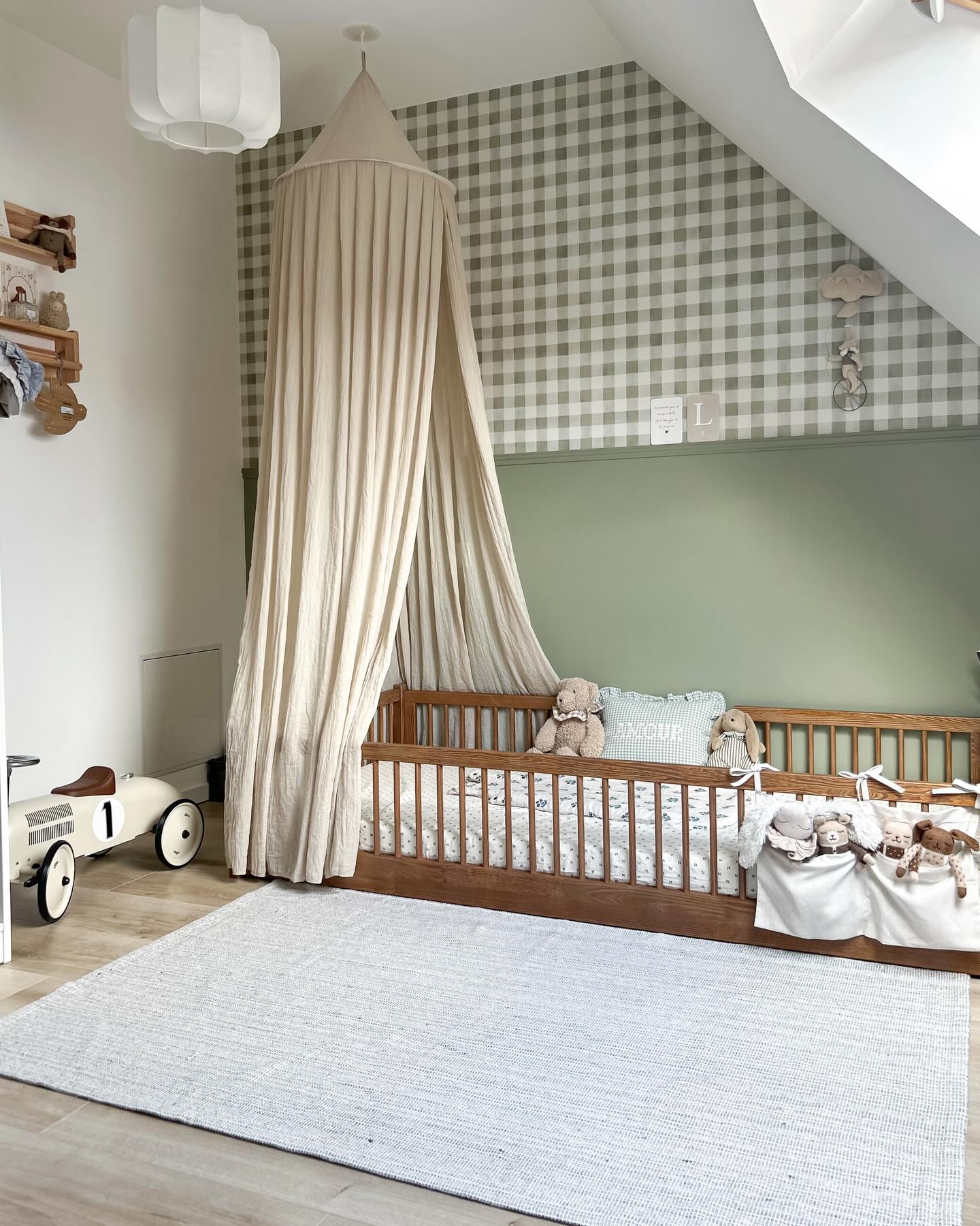 Nursery with a wooden crib, canopy, gingham wallpaper, and toy car.