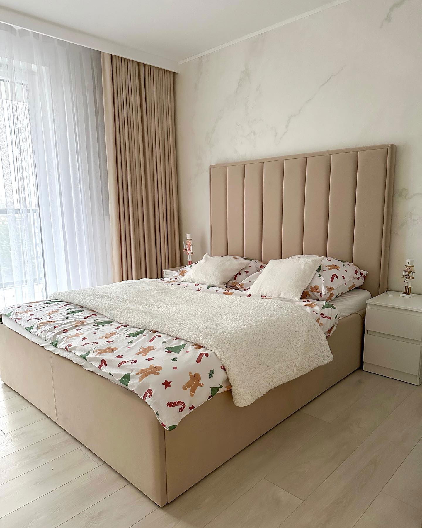Bedroom with beige upholstered bed, Christmas-themed sheets, and white sherpa blanket.