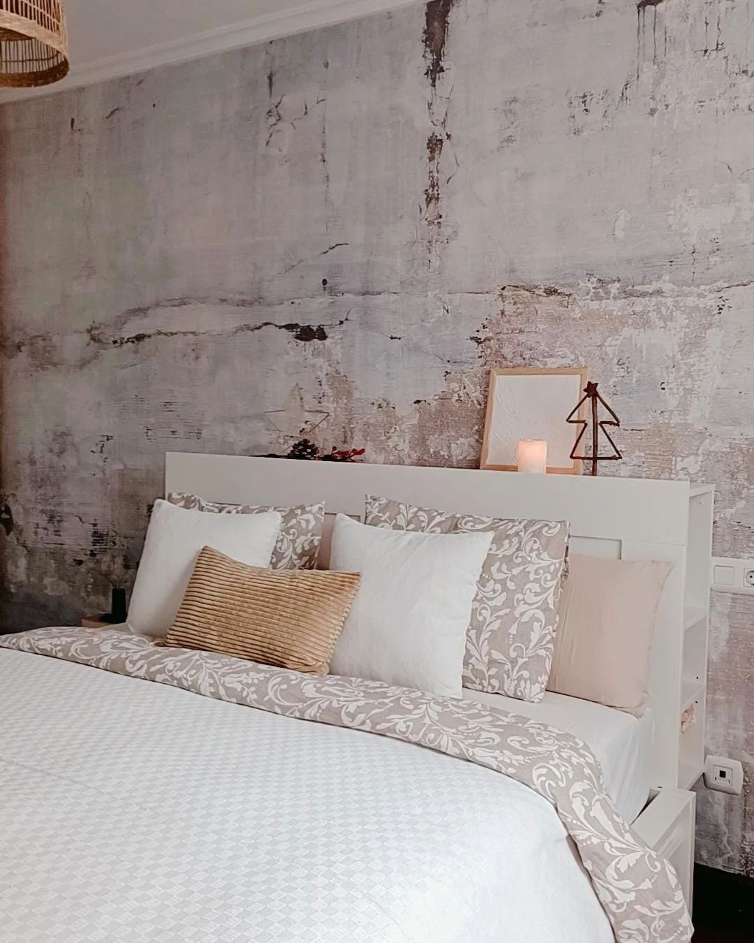 Slaapkamer met wit beddengoed, decoratieve kussens en een grijze muur met textuur. Een kleine kerstboomdecoratie staat op het hoofdeinde.