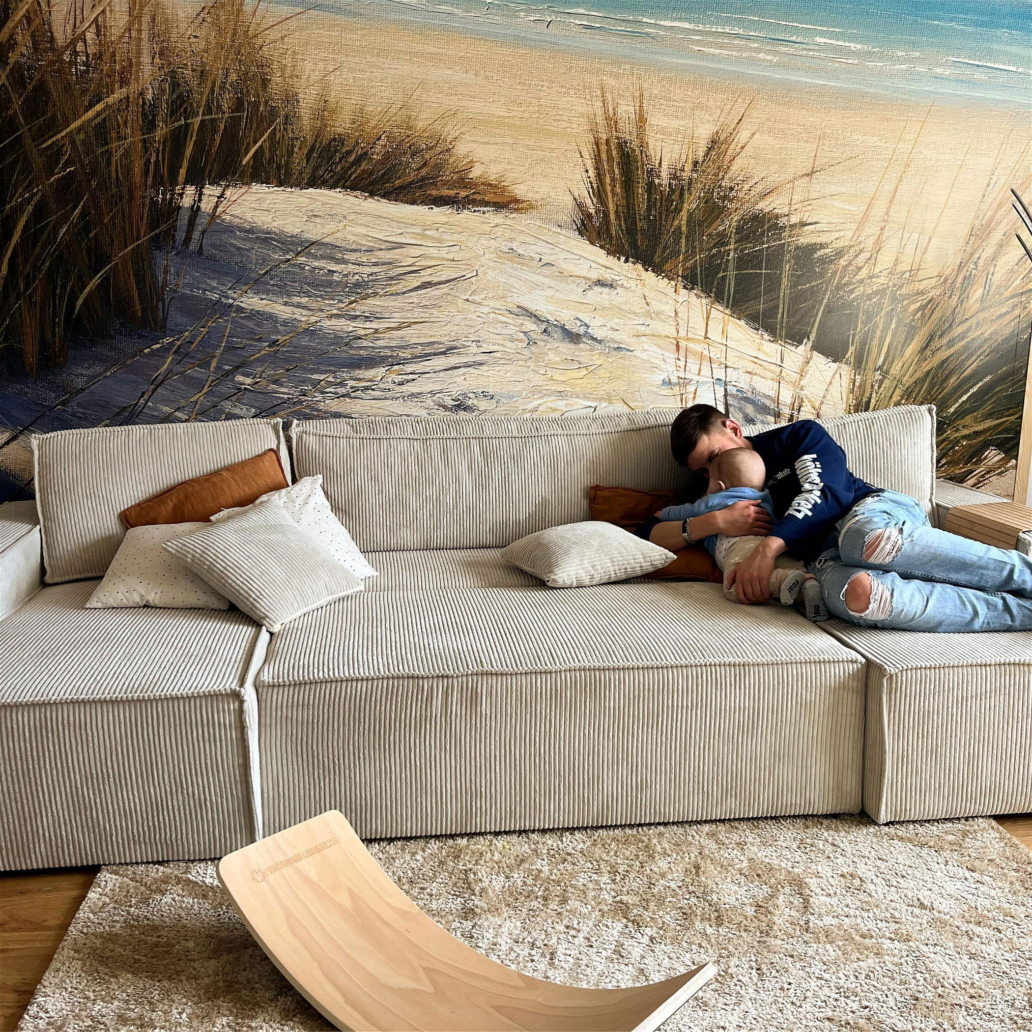 A parent and child rest on a modular, corduroy sofa with throw pillows.