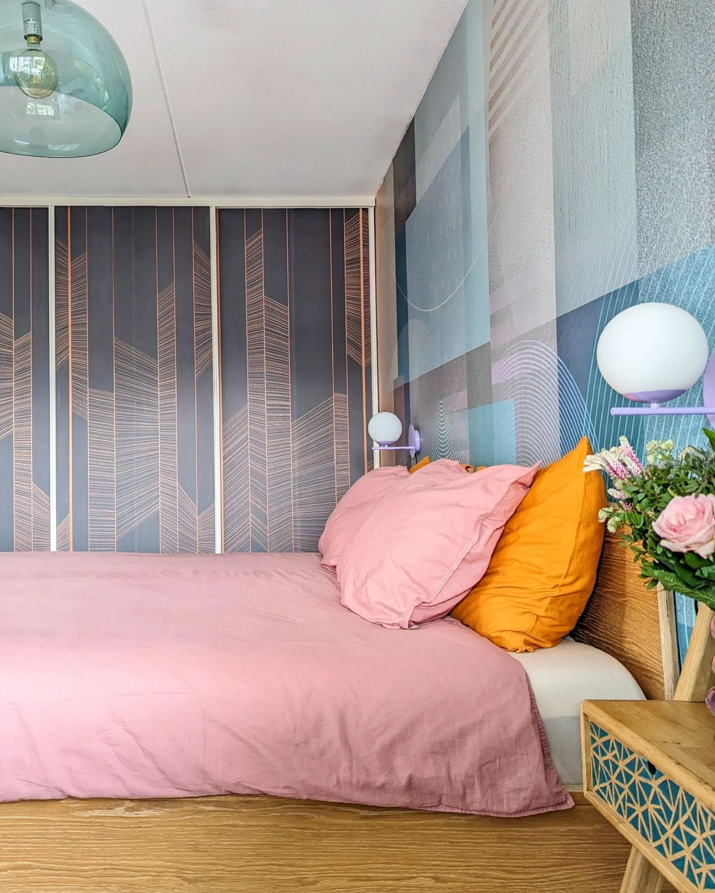 Soveværelse med pink sengetøj, orange pude og geometrisk tapet.