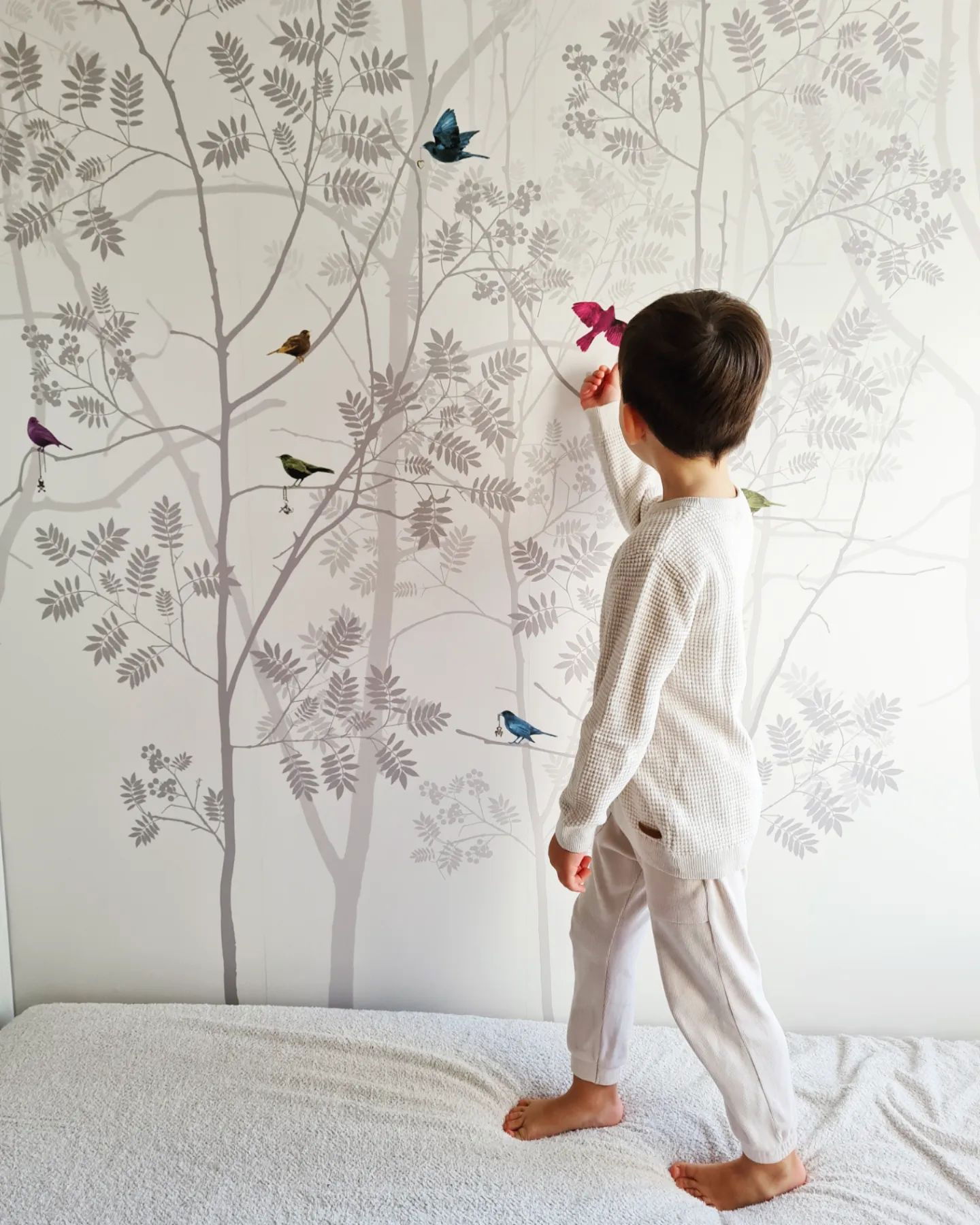 A child places a bird sticker on a wall with a tree and bird design.