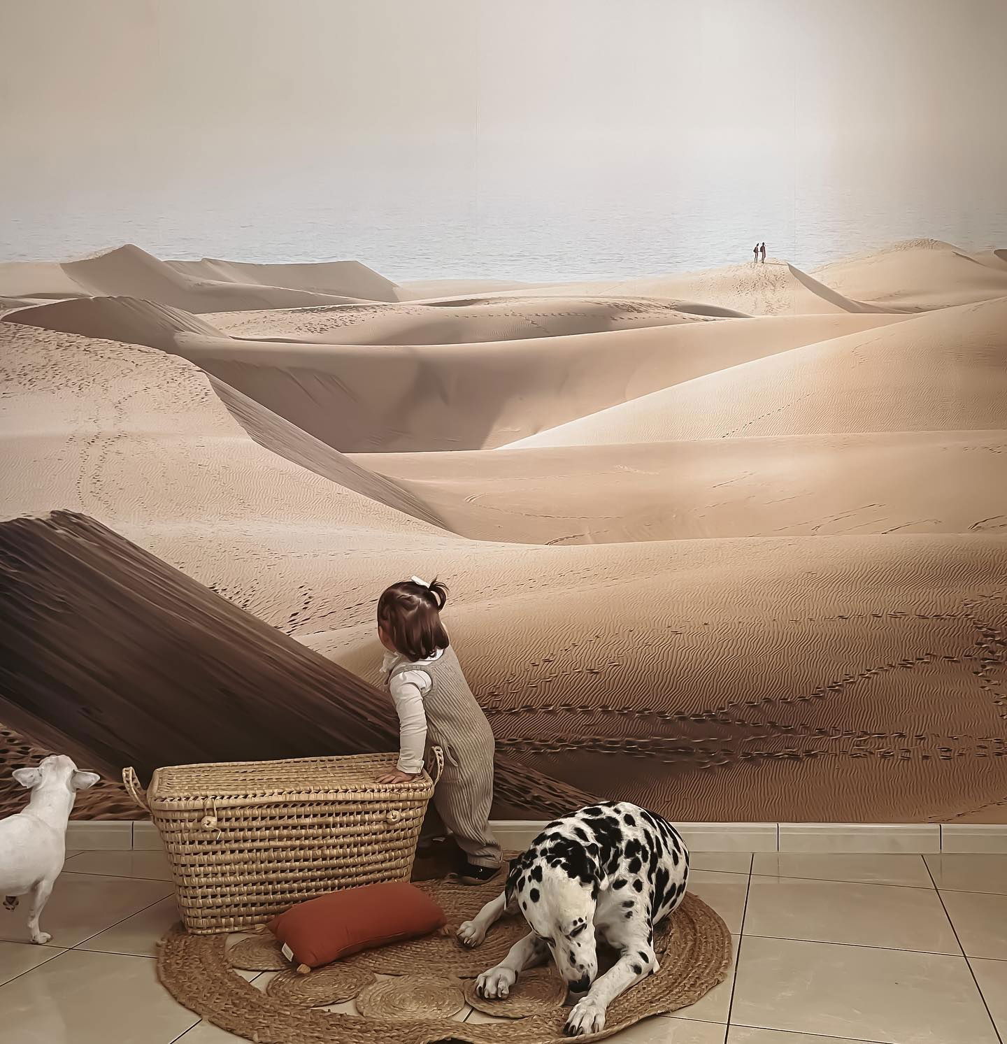 Un niño pequeño, un dálmata y un bulldog francés frente a un mural del desierto.