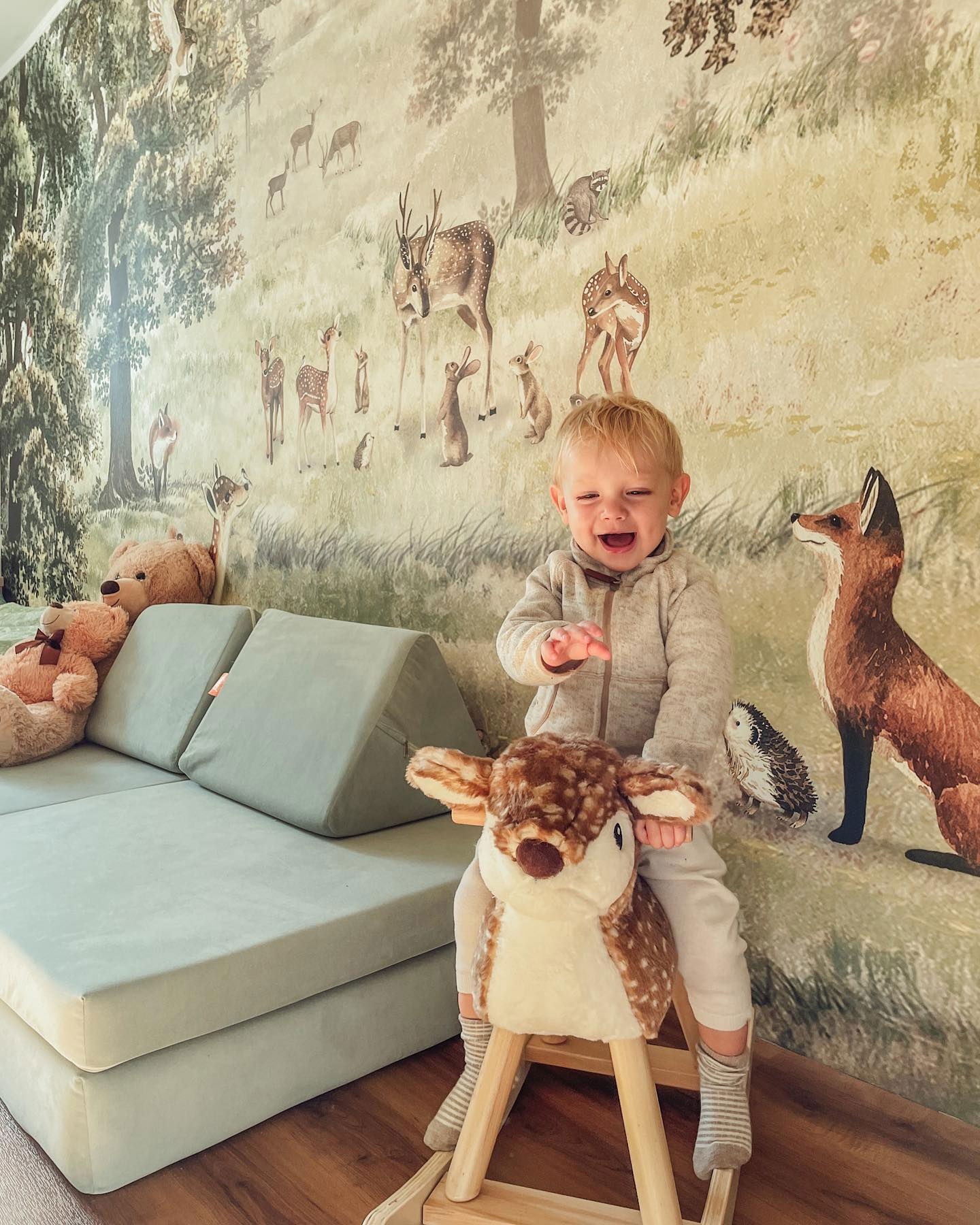 Un jeune enfant est sur un cerf à bascule en peluche dans une pièce sur le thème de la forêt.
