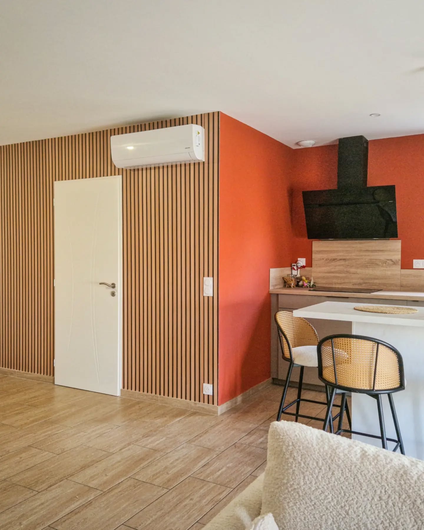 Moderne kjøkken med hvit øy, krakk med rottingrygg og oransje kontrastvegg.