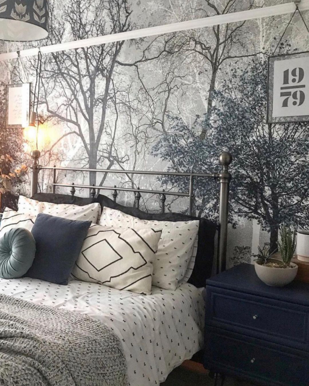 Camera da letto con letto in metallo nero, biancheria da letto fantasia, comodino blu e carta da parati a tema foresta.
