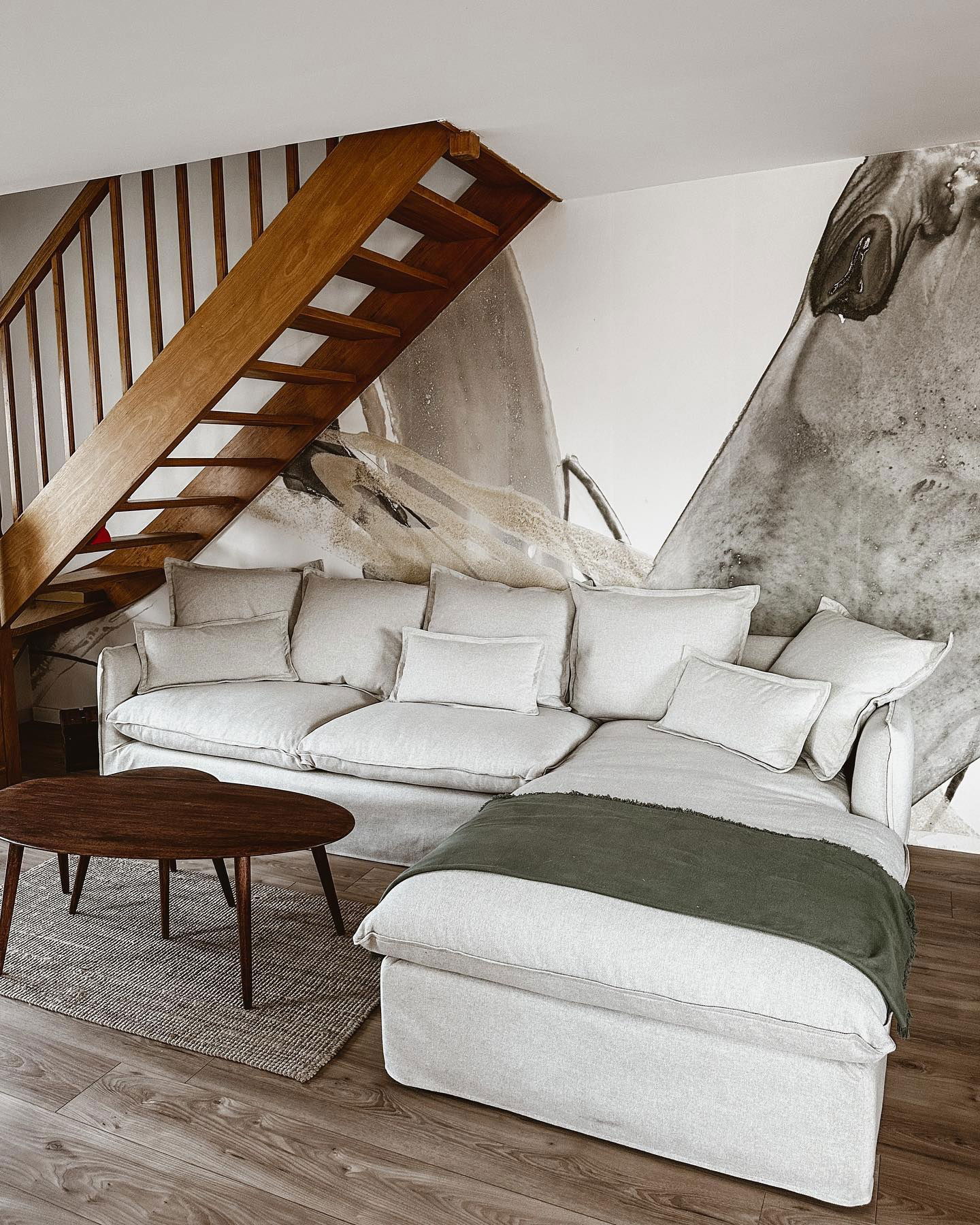 Living room with white sofa, wood stairs, and abstract wall art.
