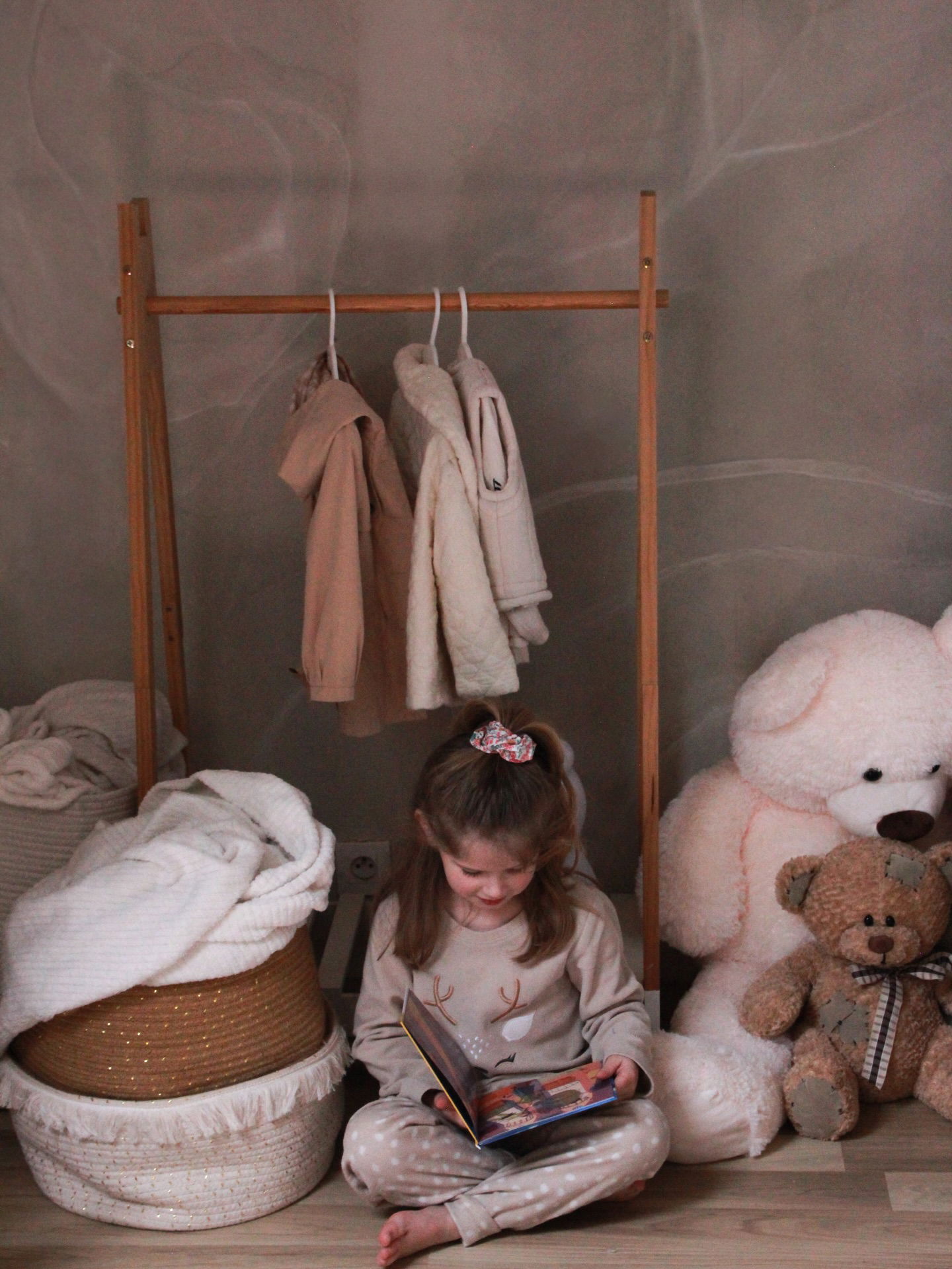 Child reading in a room with teddy bears and a clothing rack.
