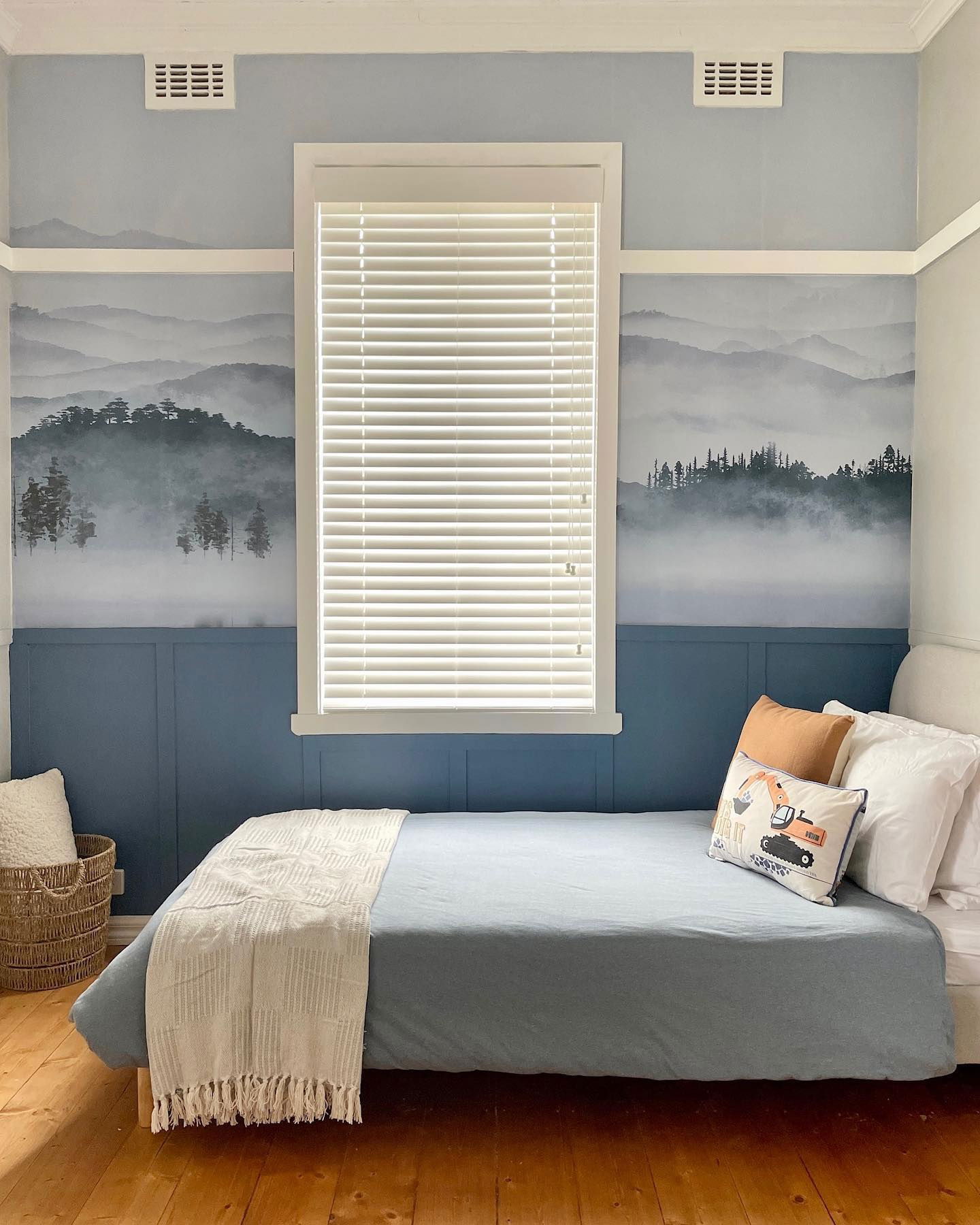 Bedroom with blue walls, mountain mural, and a bed with blue duvet and decorative pillows.