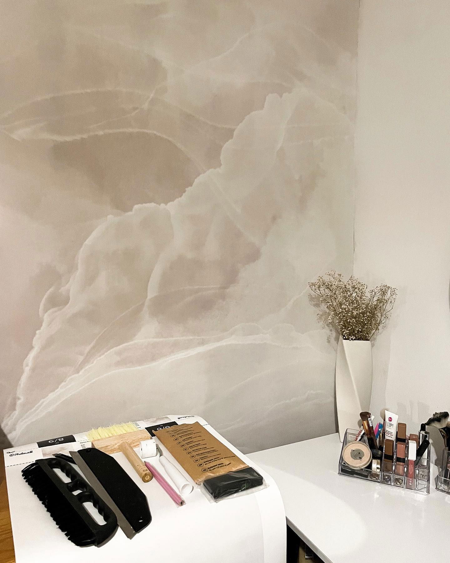 Interno con carta da parati a motivi marmorei, strumenti e trucco su una scrivania bianca.