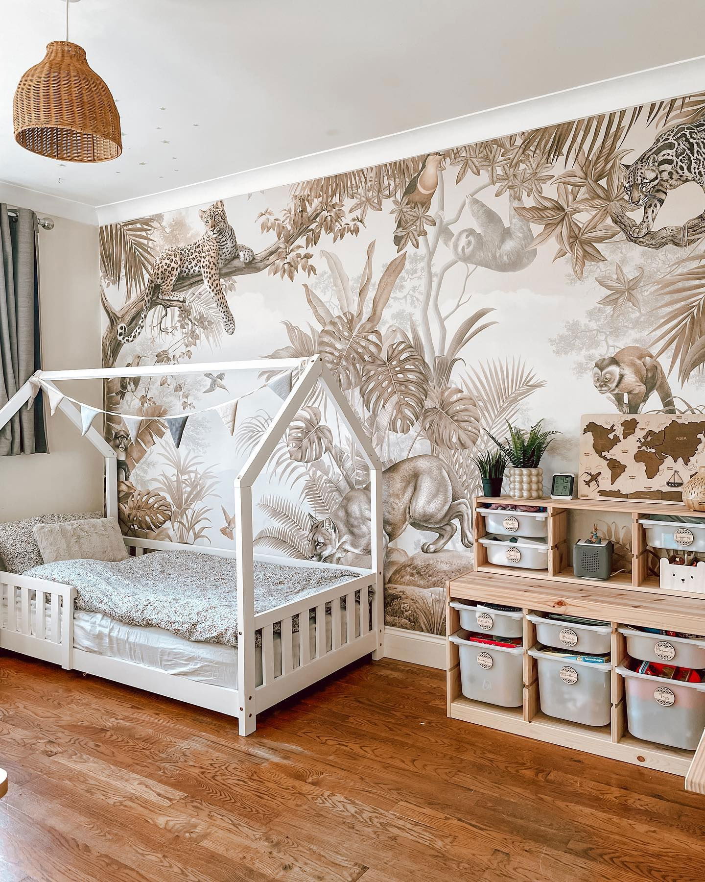 Child's bedroom with jungle mural, white house frame bed, and wooden storage unit with labeled bins.