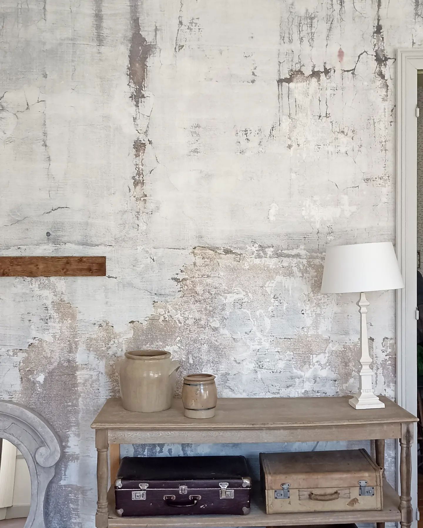 Rustiek interieur met verweerde muur, vintage koffers en aardewerk in neutrale tinten op een houten consoletafel.