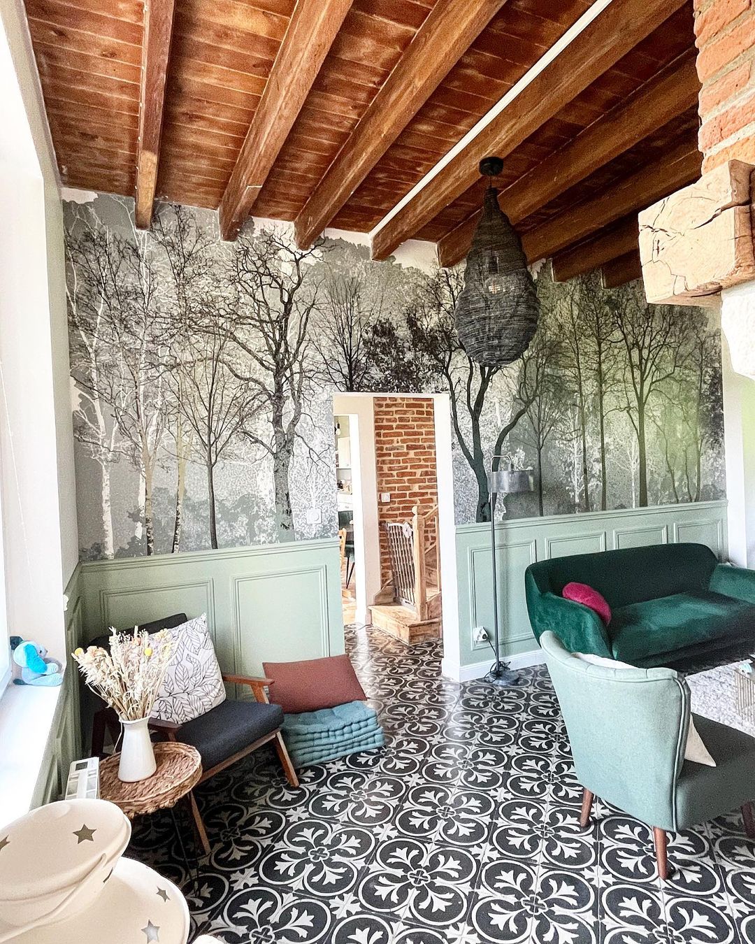 Eclectic living room with forest wallpaper, green wainscoting, and black and white patterned tile.
