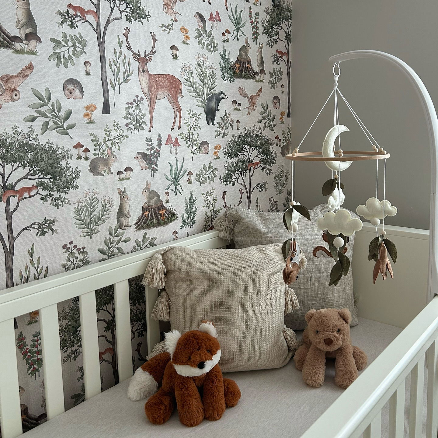 Nursery with woodland wallpaper, white crib, and mobile with moon and cloud details.