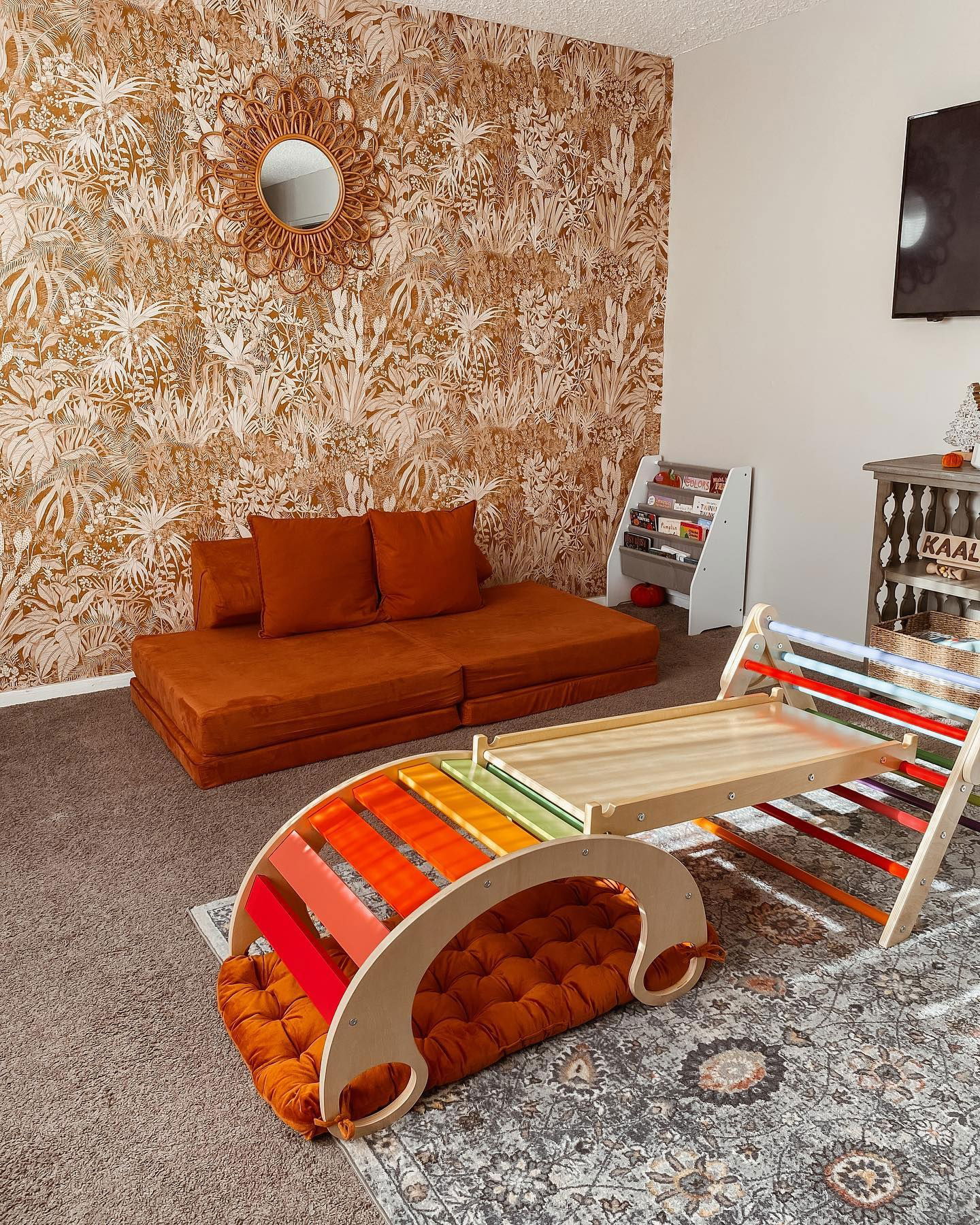 Playroom with orange Nugget couch, floral wallpaper, and wooden climbing structure with colorful rungs.