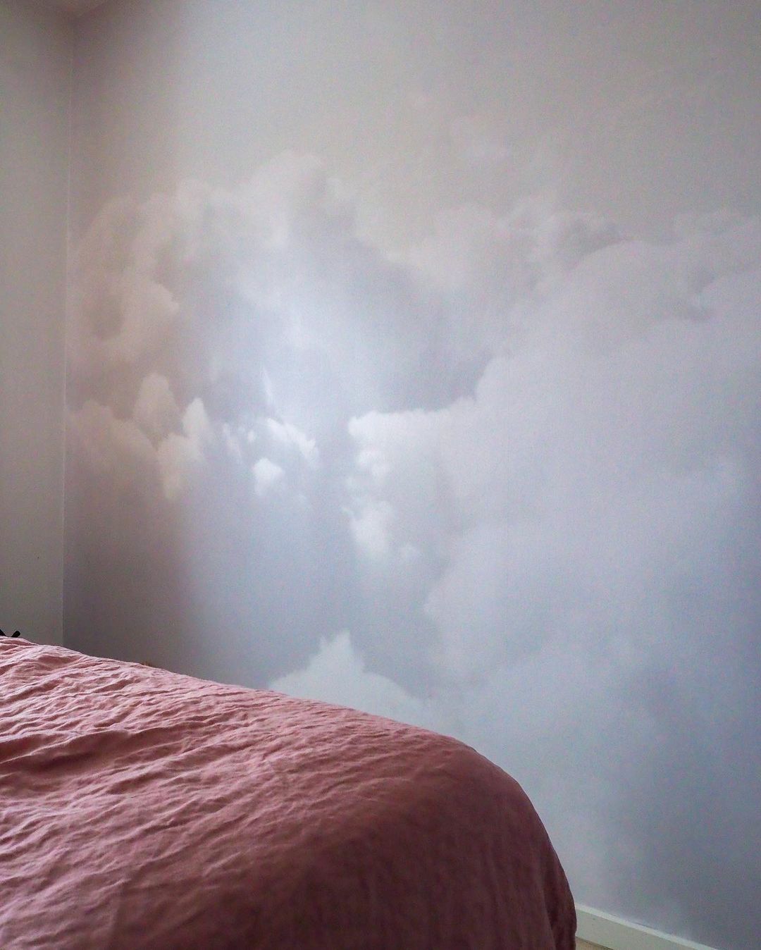 Bedroom with pink bedspread and wall mural of clouds.