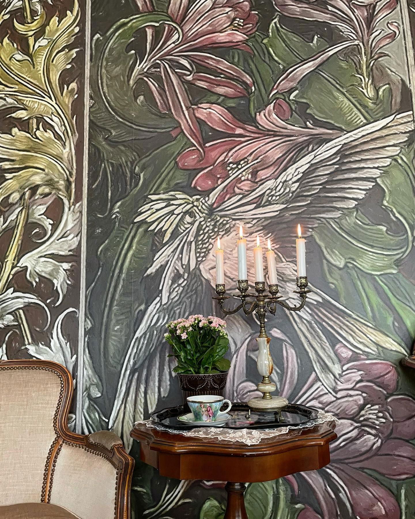 Vintage-rum med blommiga tapeter, tända ljus och en tekopp på ett litet bord.