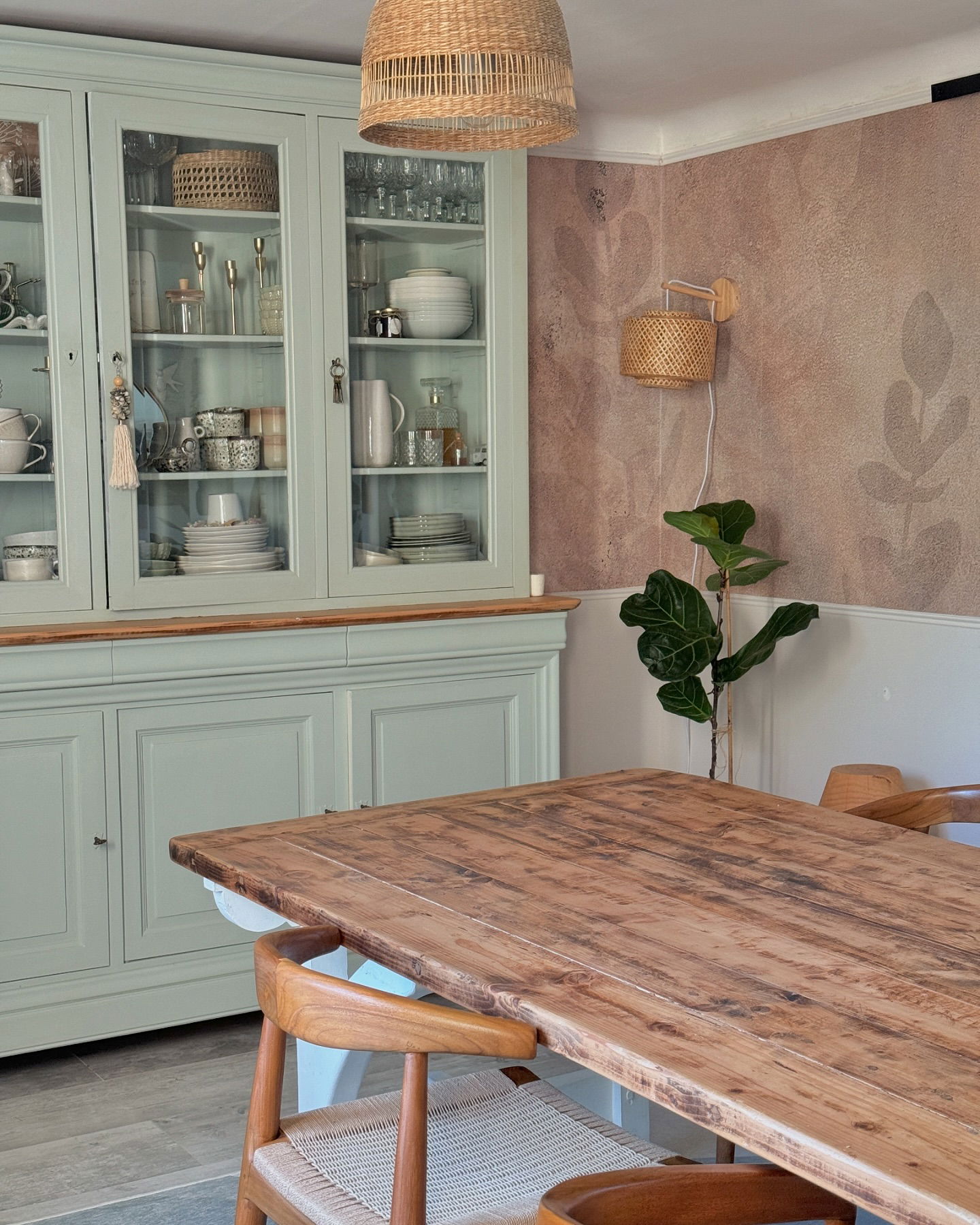Salle à manger avec un vaisselier bleu clair, une table et des chaises en bois, et des luminaires tissés.
