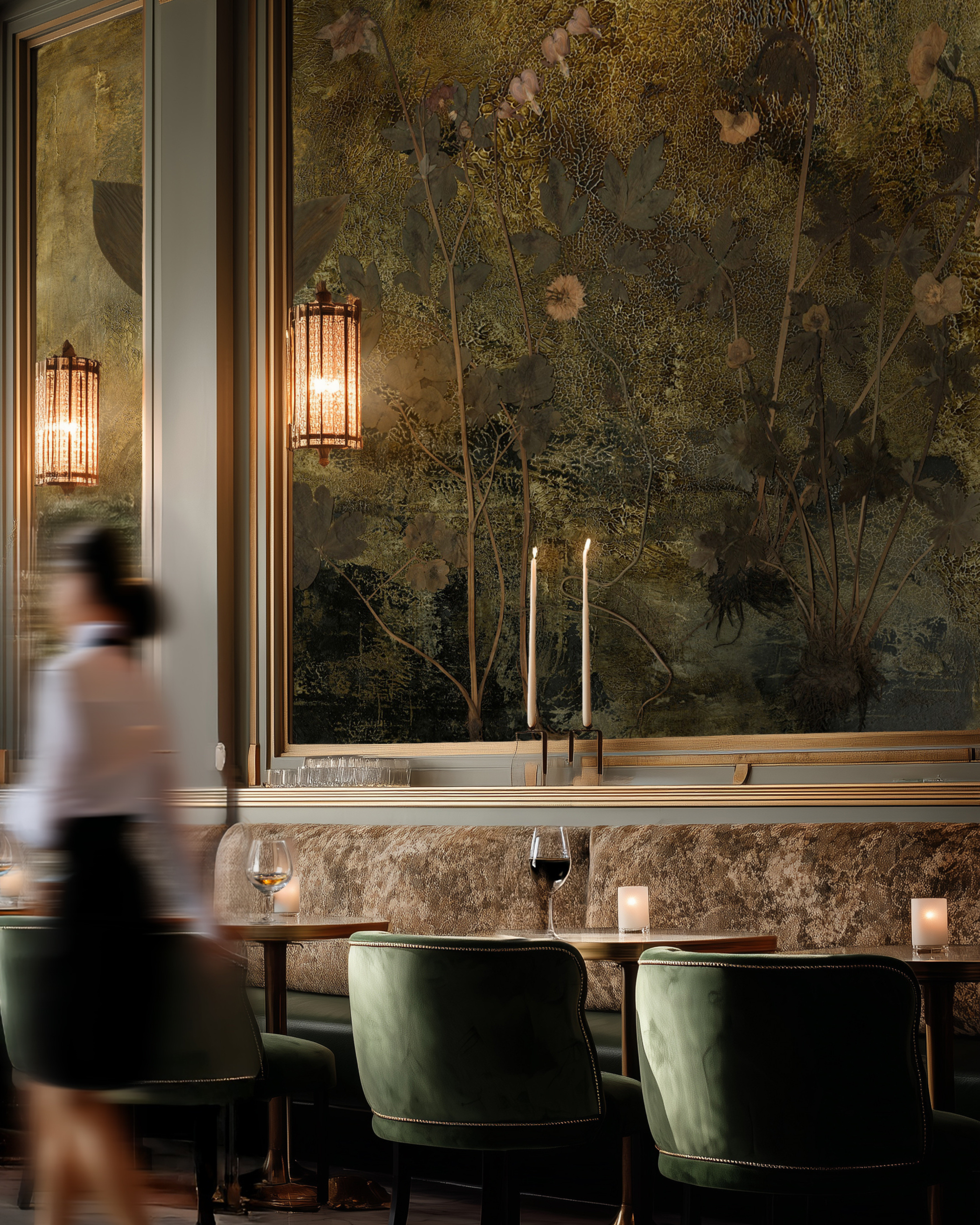 Elegant restaurant interior with floral wallpaper, green velvet chairs, and a blurred server.