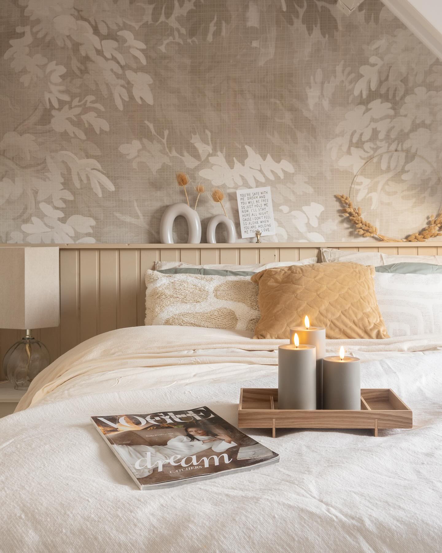 Bedroom scene with Vogue magazine, lit candles on a tray, and leaf-patterned wallpaper.