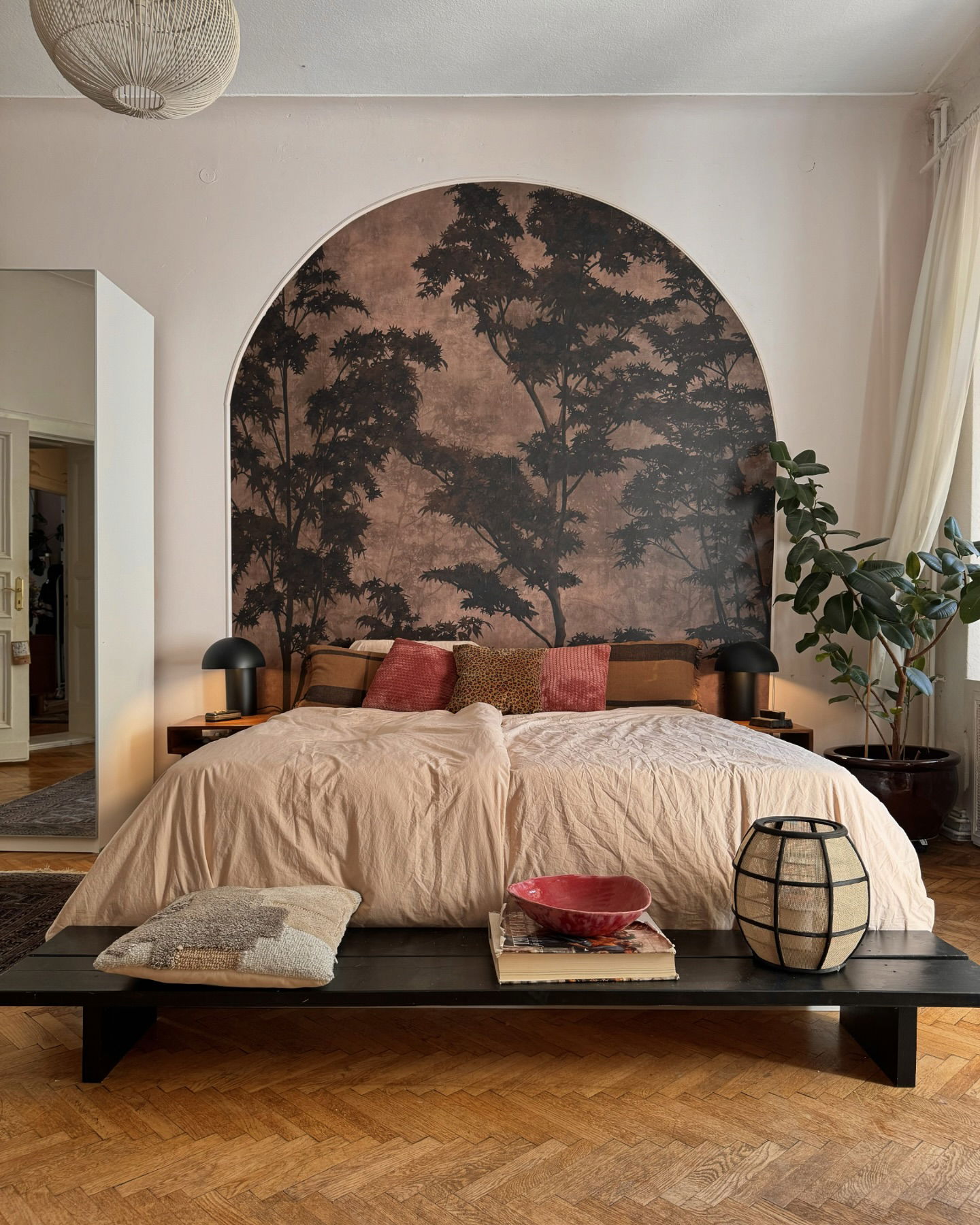 Bedroom with salmon bedding, tree mural in archway, and black bench.