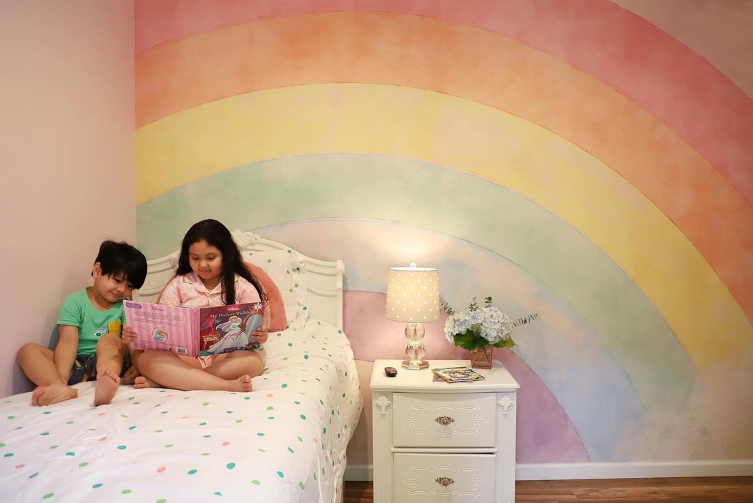 Zwei Kinder lesen ein Disney-Buch auf einem gepunkteten Bett vor einer regenbogenfarbenen Wand.
