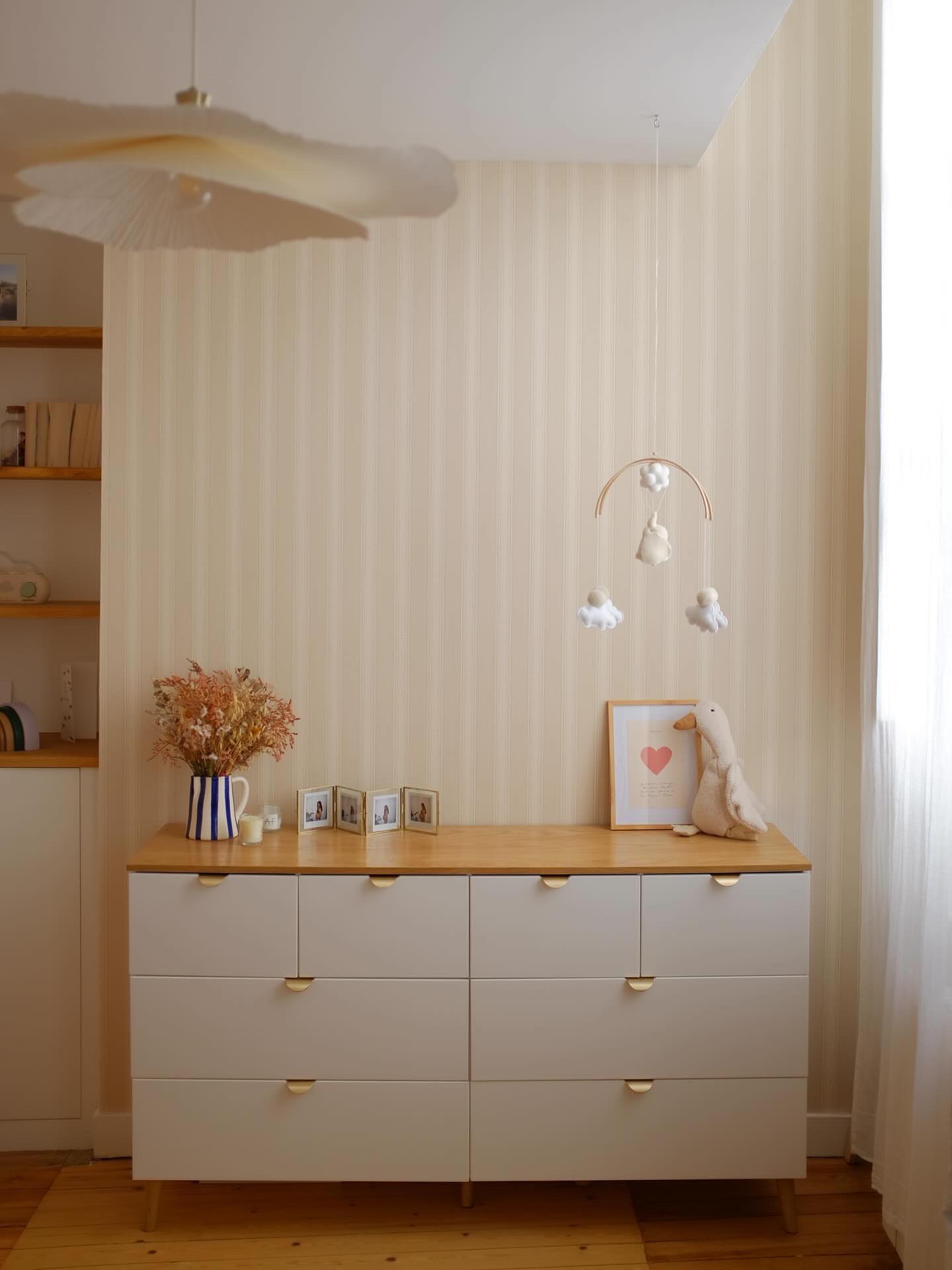 Nursery with white dresser, wooden top, and gold pulls. A mobile hangs above, and a plush duck sits on top.