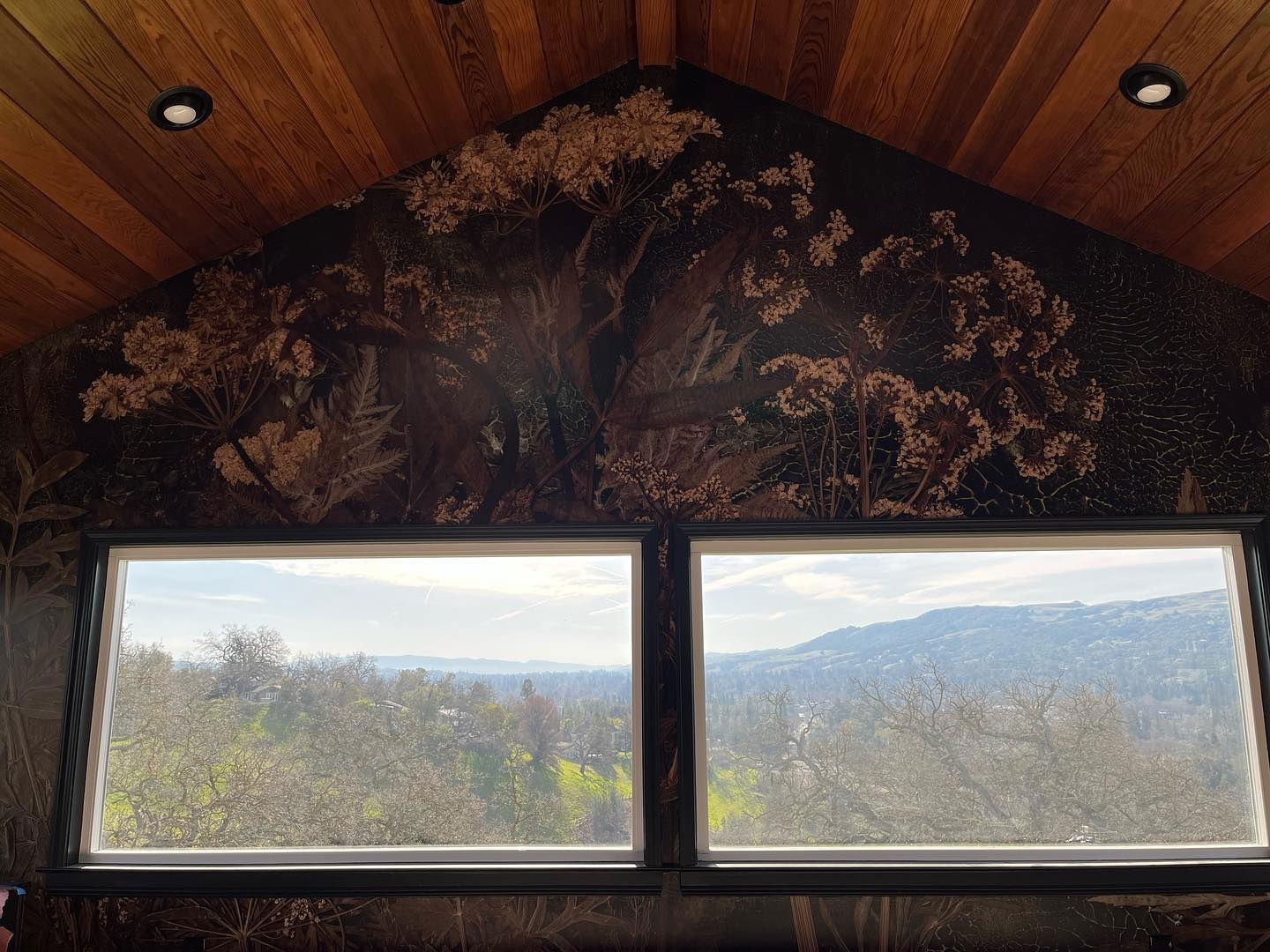 Innenansicht von zwei Fenstern mit Blick auf ein Tal, Blumentapete und Holzdecke.