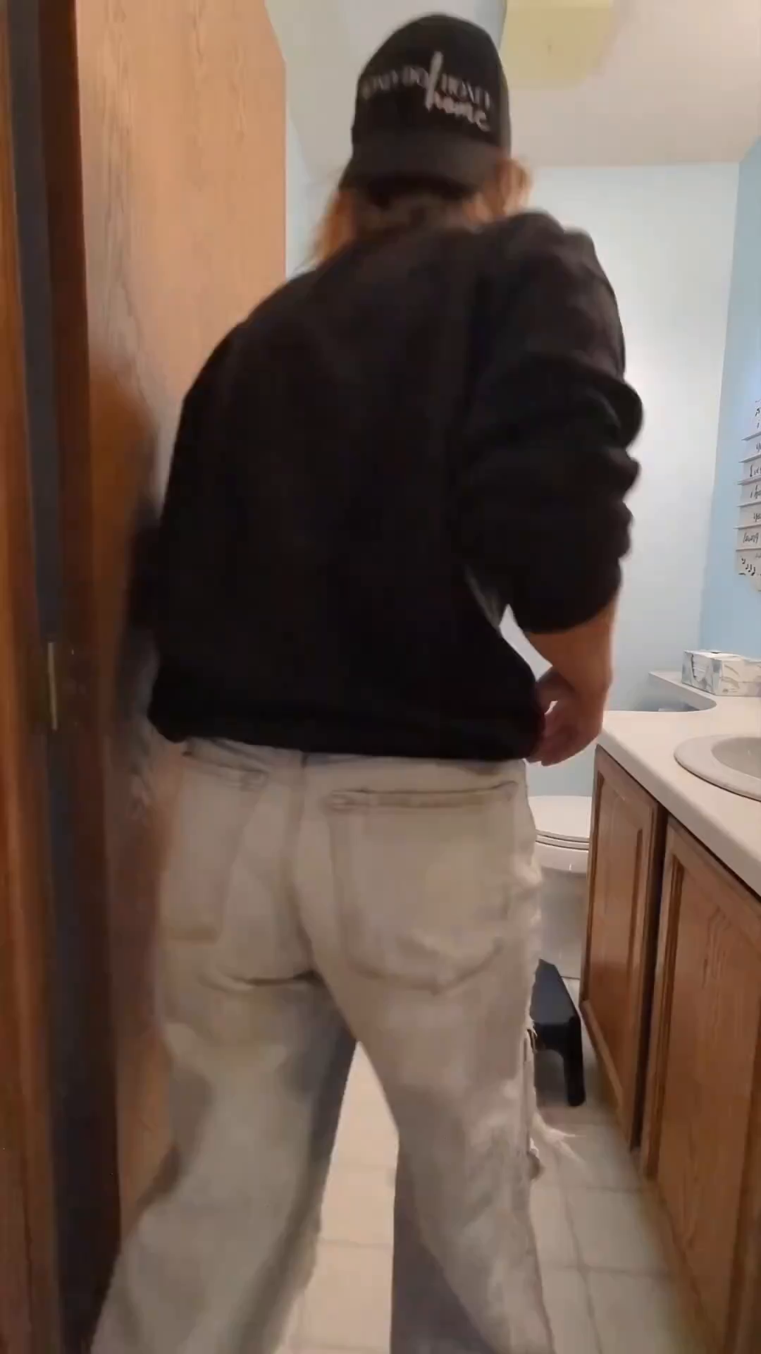 Person in black sweatshirt and light jeans, wearing a "Good Dog Home" baseball cap.