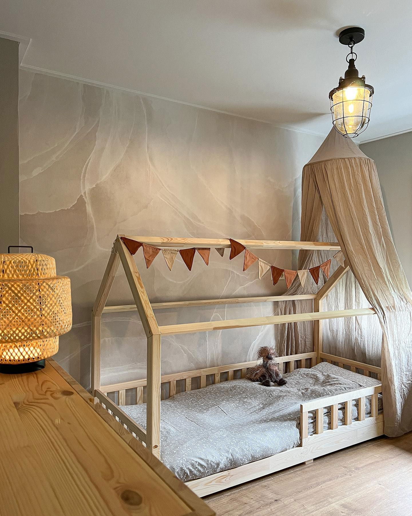 Camera da letto per bambini con letto a casetta in legno, baldacchino e banner a pennone. Lampada in vimini sul comò.