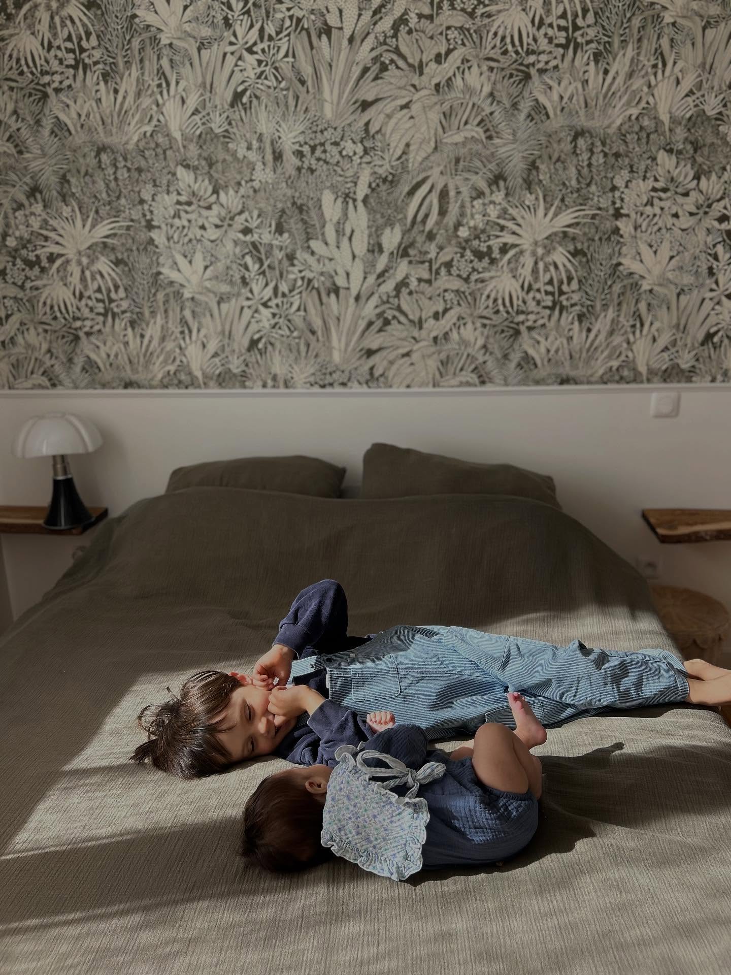 Two boys on a bed with a botanical print wallpaper