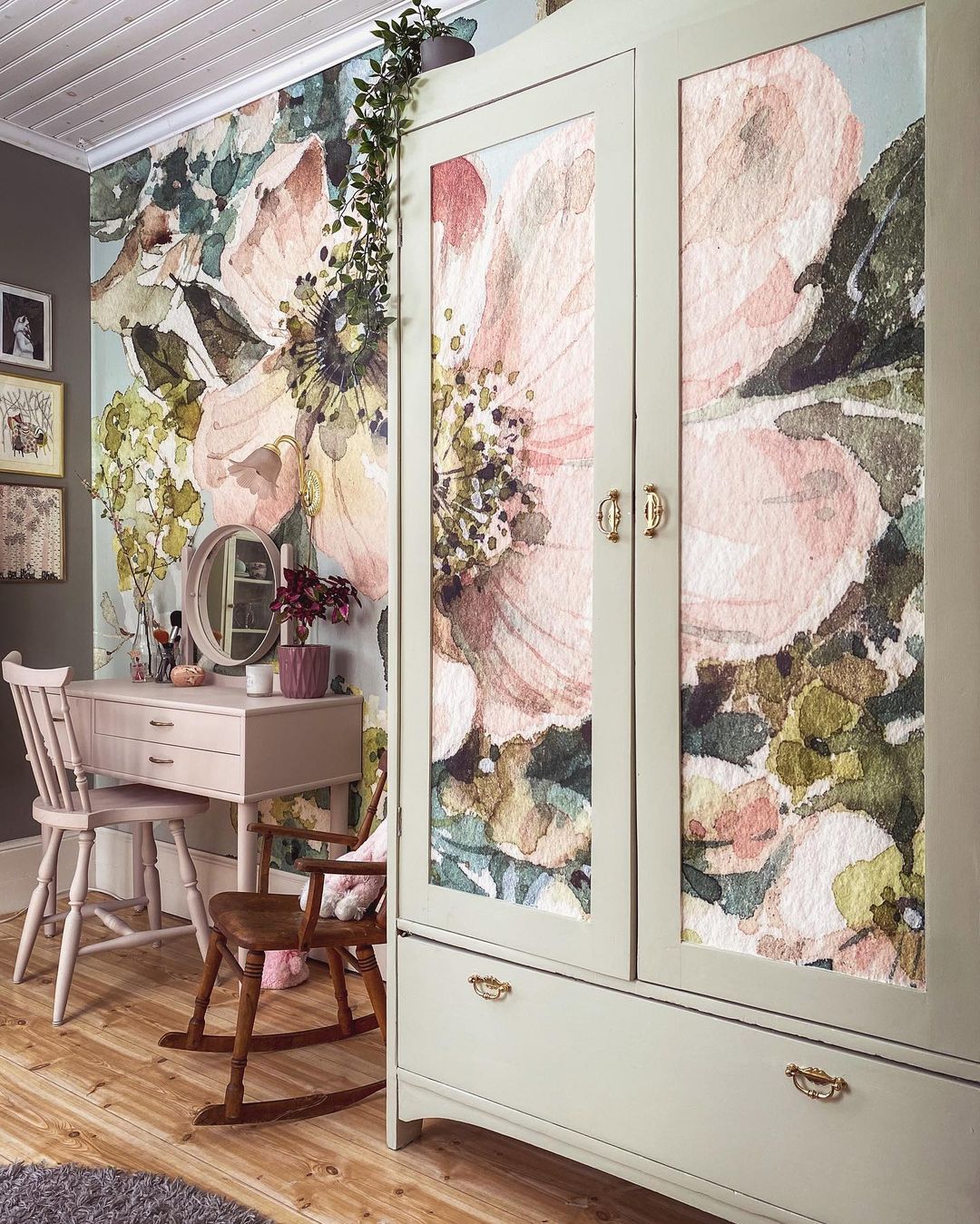 Schlafzimmer mit floraler Tapete, rosa Waschtisch und salbeigrünem Kleiderschrank mit floralen Paneelen.