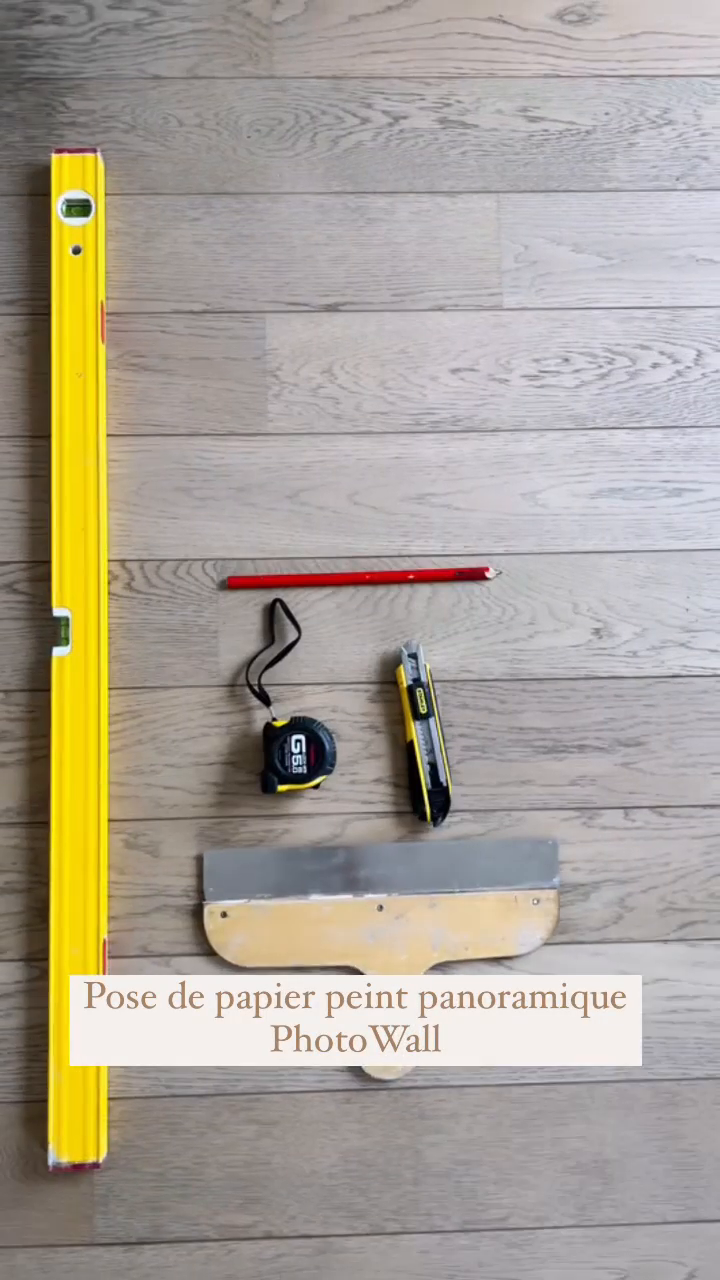 Overhead shot of tools for wallpapering: level, pencil, tape measure, utility knife, and putty knife.